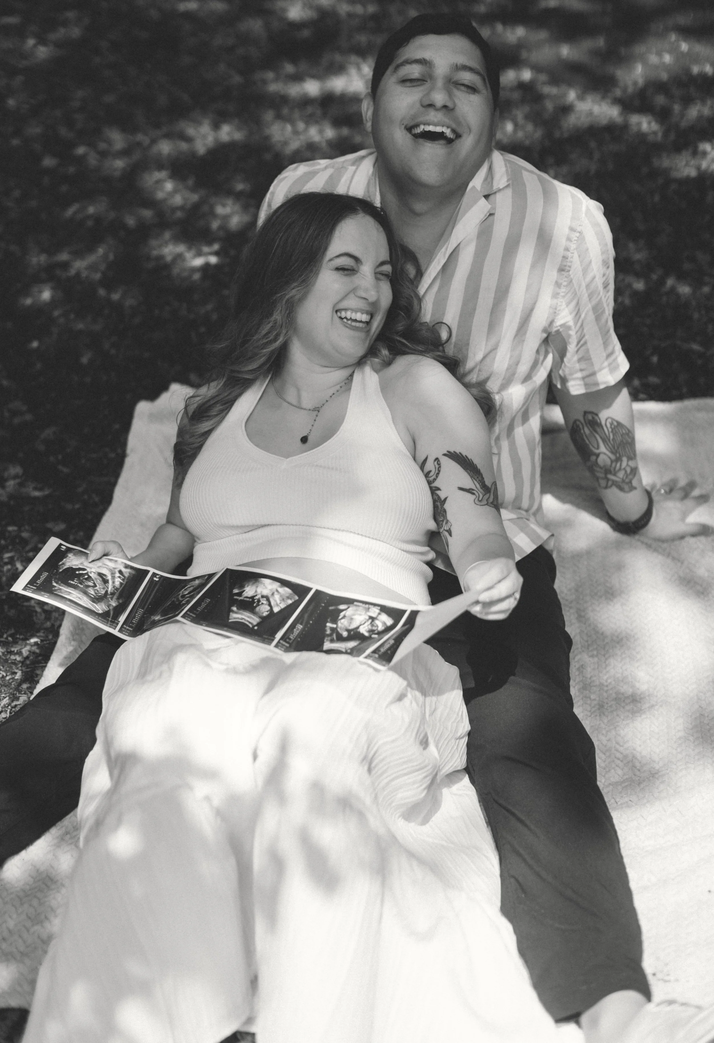 Expecting mother outdoors while holding baby ultrasound photos.