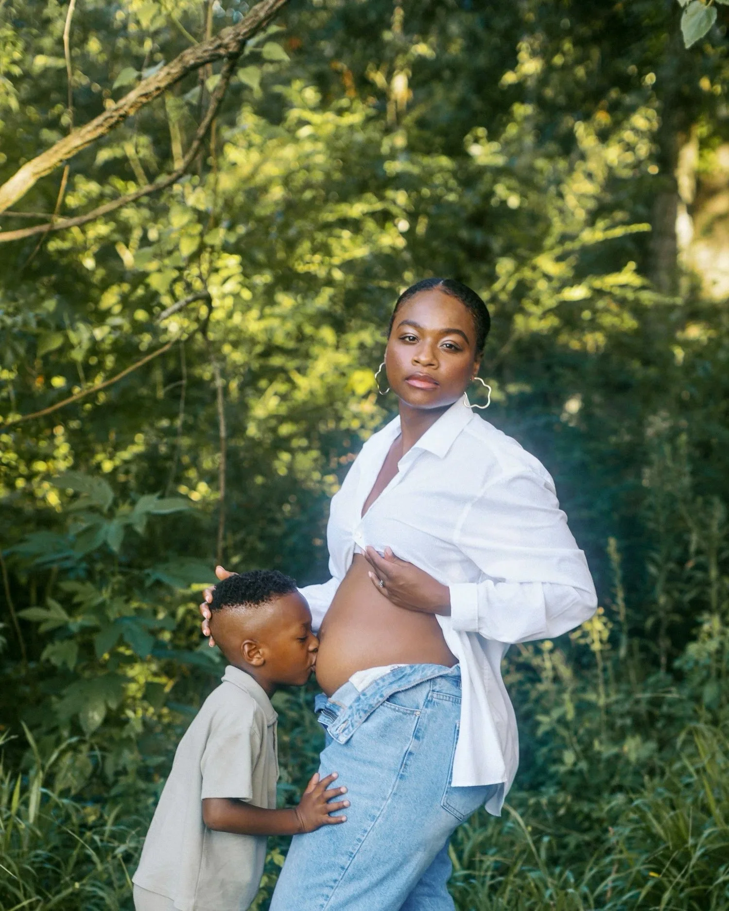 Pregnant mother cradling her belly during a golden hour maternity session in New Orleans, surrounded by lush greenery and soft Southern light.