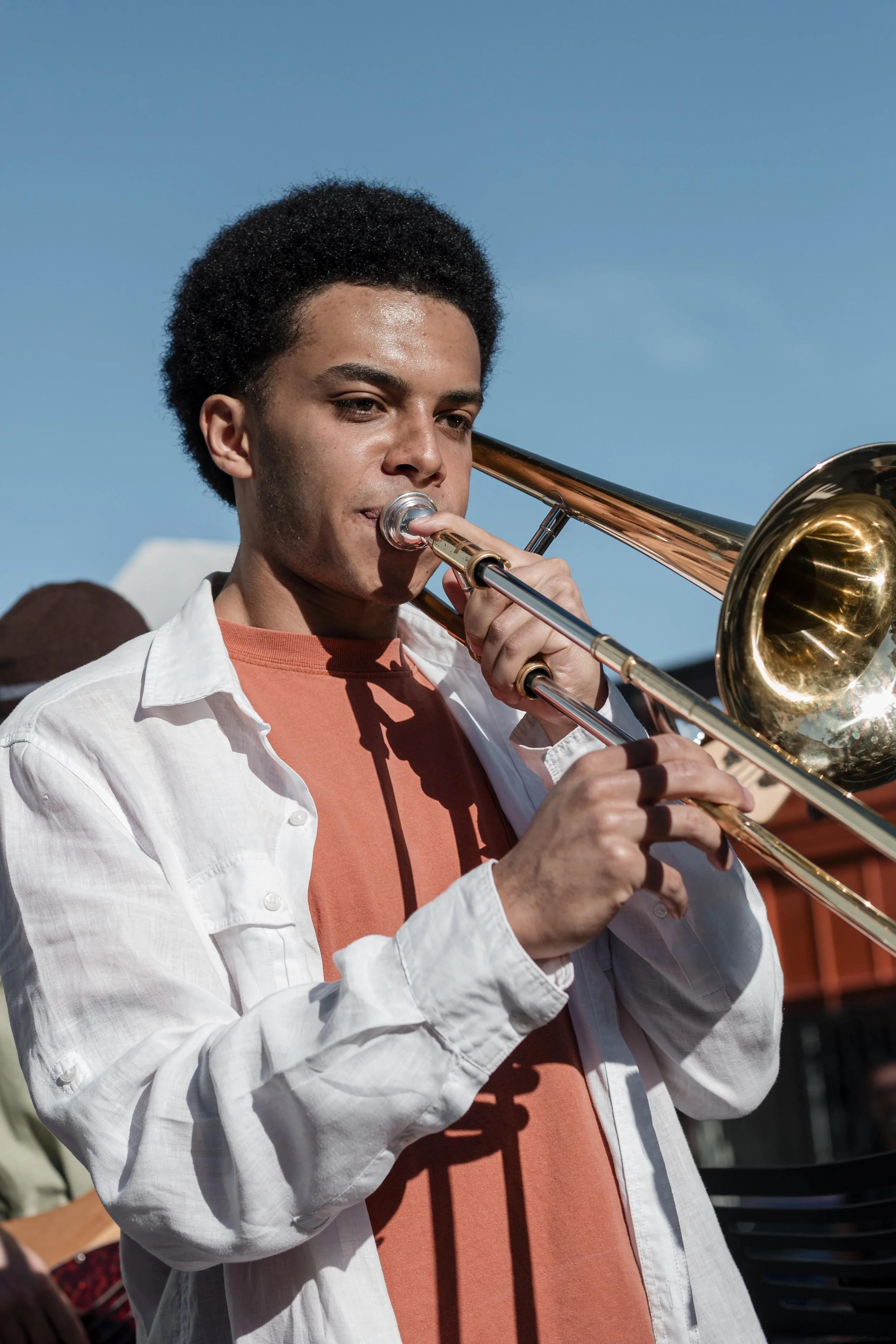 Young man playing the trombone outdoors under a clear blue sky.