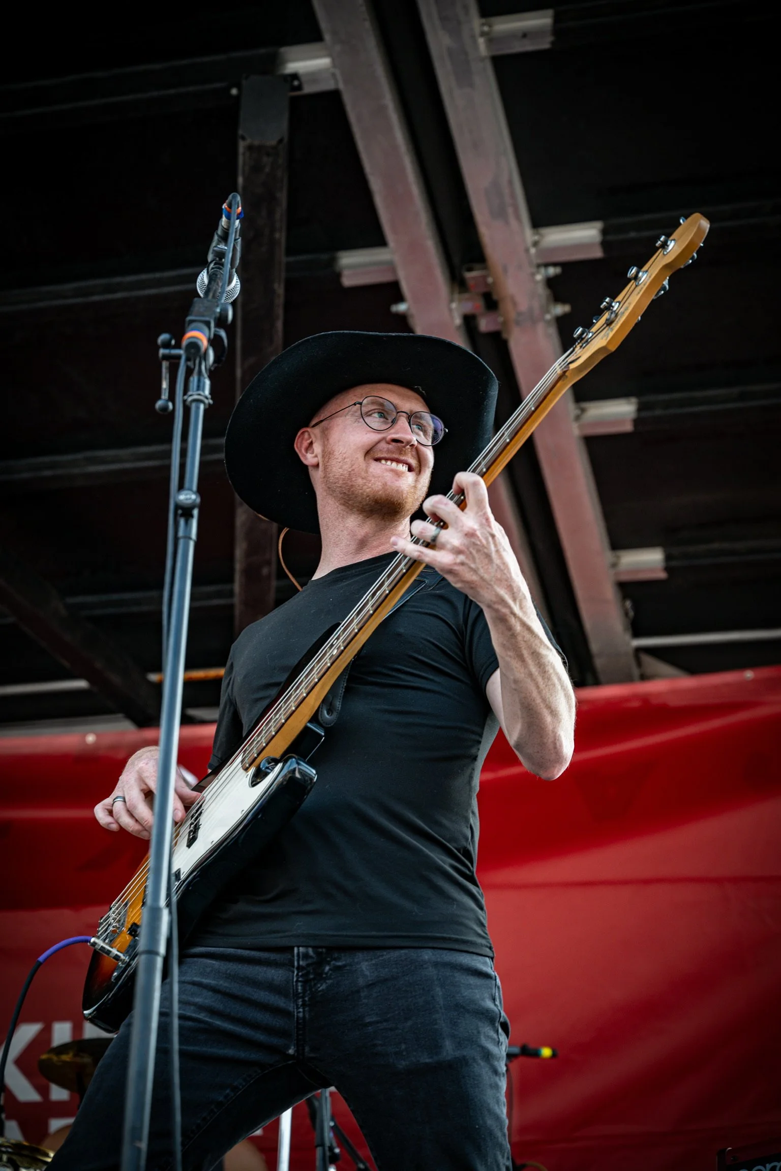 A black and white photo of a man wearing glasses, a cap, and hoodie, playing an electric guitar.