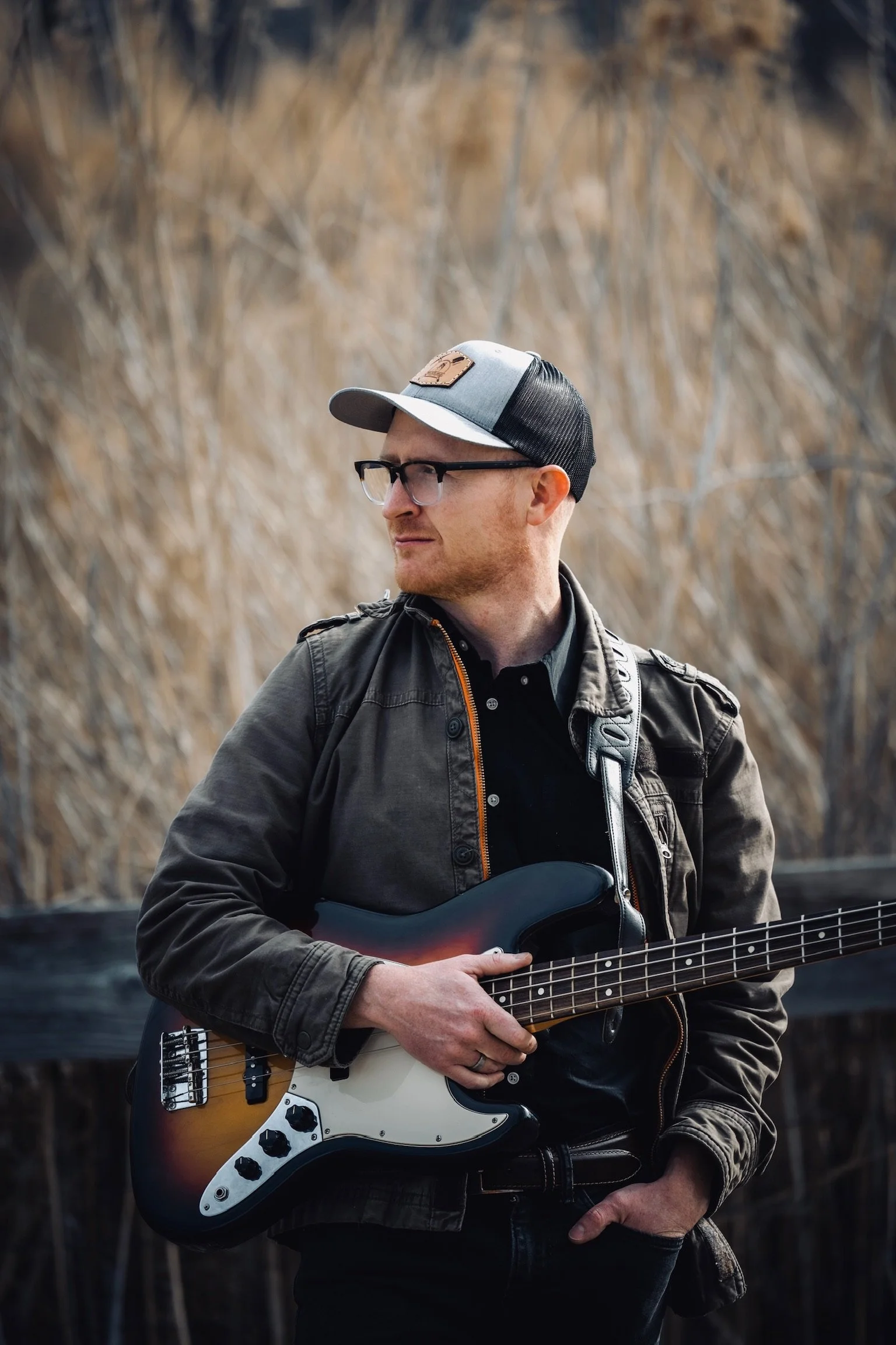 A black and white photo of a man wearing glasses, a cap, and hoodie, playing an electric guitar.