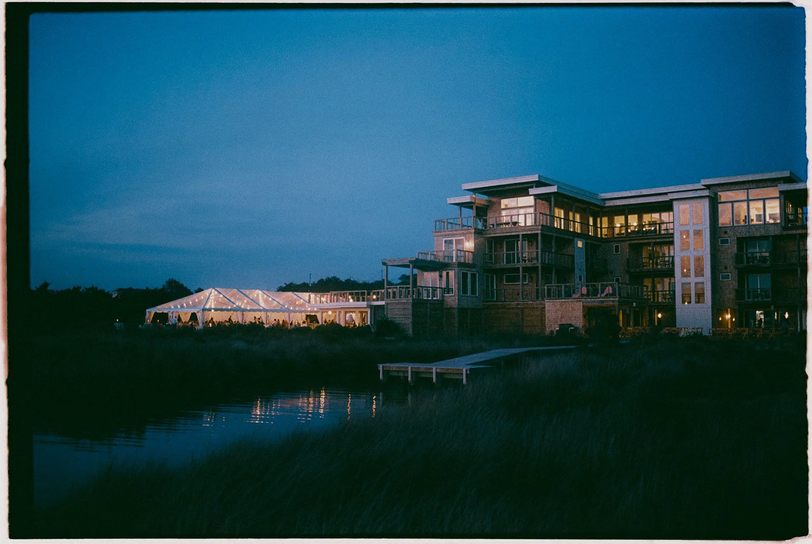 The flagship house at Edgecamp at dusk with the wedding tent lit on the lawn beside the Pamlico Sound.