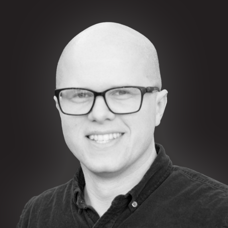 Black and white portrait of a smiling man with glasses, wearing a collared shirt.