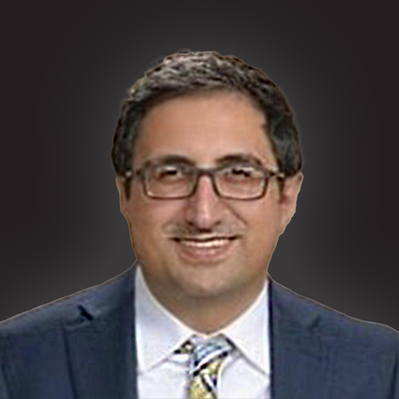 Professional headshot of a man wearing glasses, a dark suit, a white shirt, and a striped tie, smiling against a dark background.
