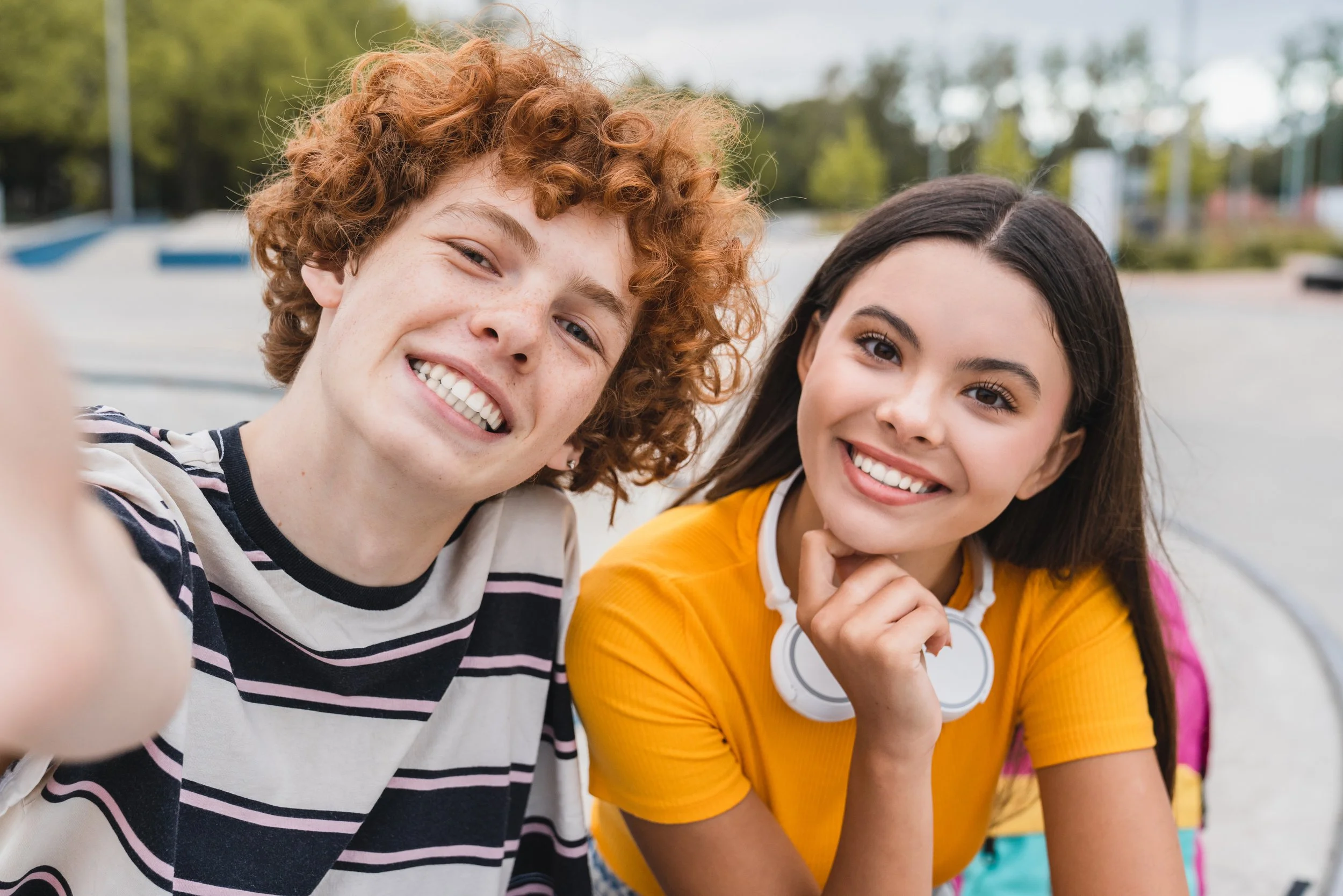 Two young adults taking a selfie outdoors at a skate park on a cloudy day.