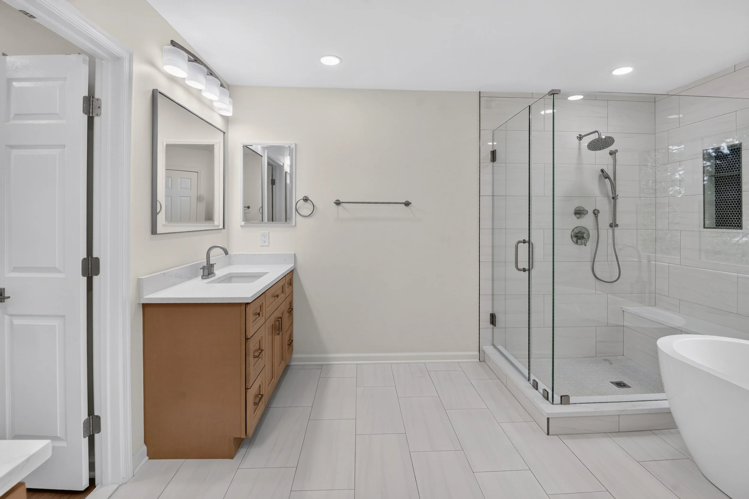 Bathroom with a double vanity mirror, a sink, light fixture, toilet, walk-in shower with glass enclosure, tiled walls and floor, and a white ceiling.