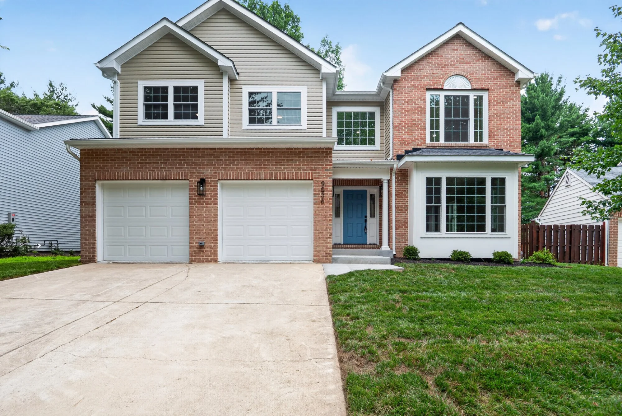 Two-story suburban house with a brick and beige siding exterior, a double garage, a blue front door, and multiple large windows, with a driveway and small front lawn.