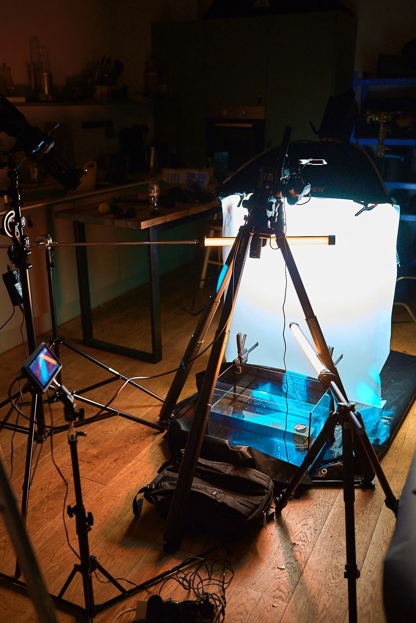A scientific setup with cameras, tripods, and lighting equipment focused on a water tank with a clear container, surrounded by various equipment and cables in a dimly lit room.