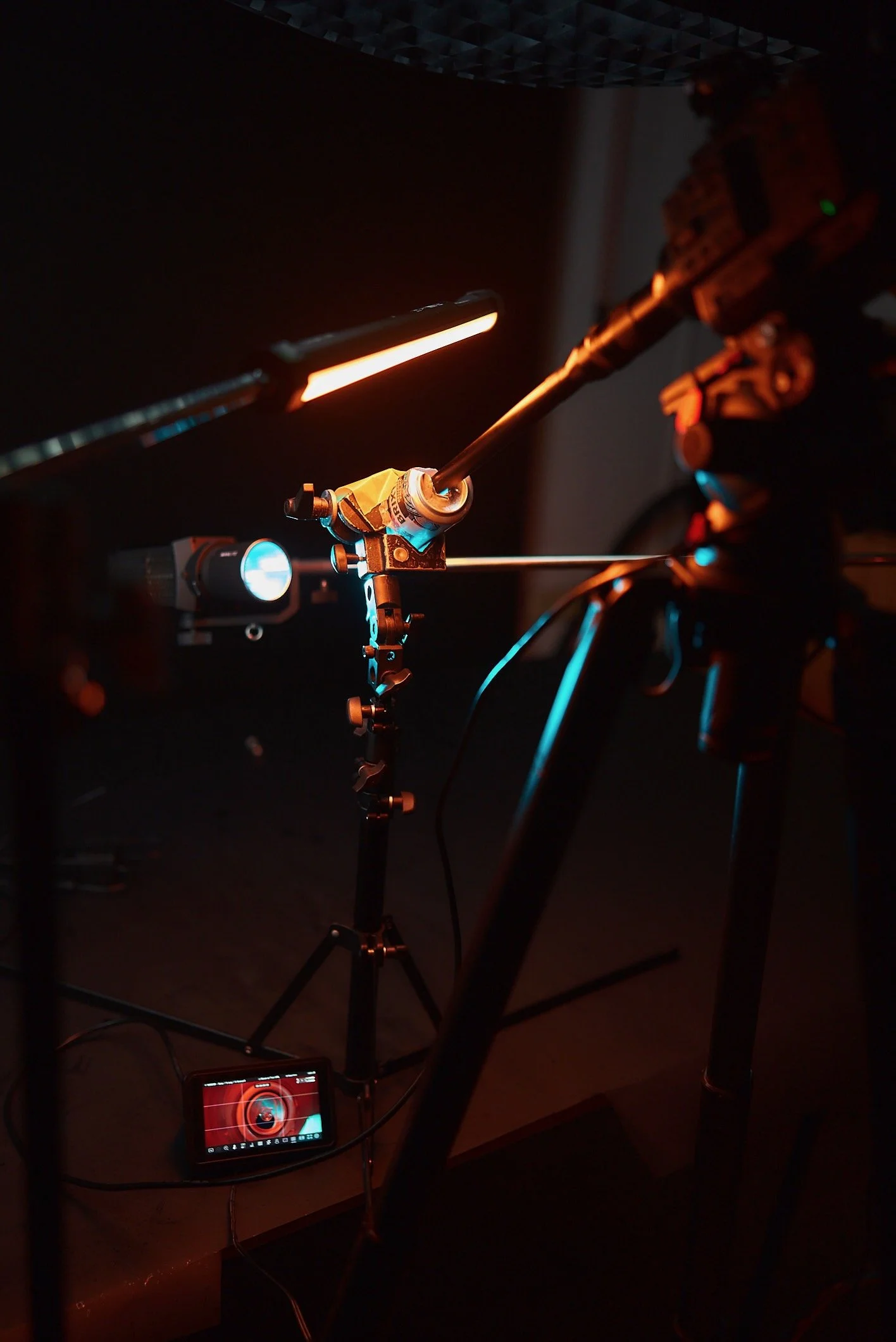 A close-up of a robotics or engineering setup with a robotic arm, tools, and equipment illuminated by orange and blue lights in a dark environment.