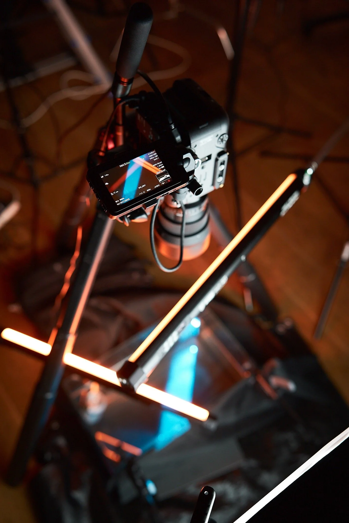 Lighting equipment and camera mounted on a tripod setup, with LED light bars and a small monitor displaying a color graph, in a dark studio setting.