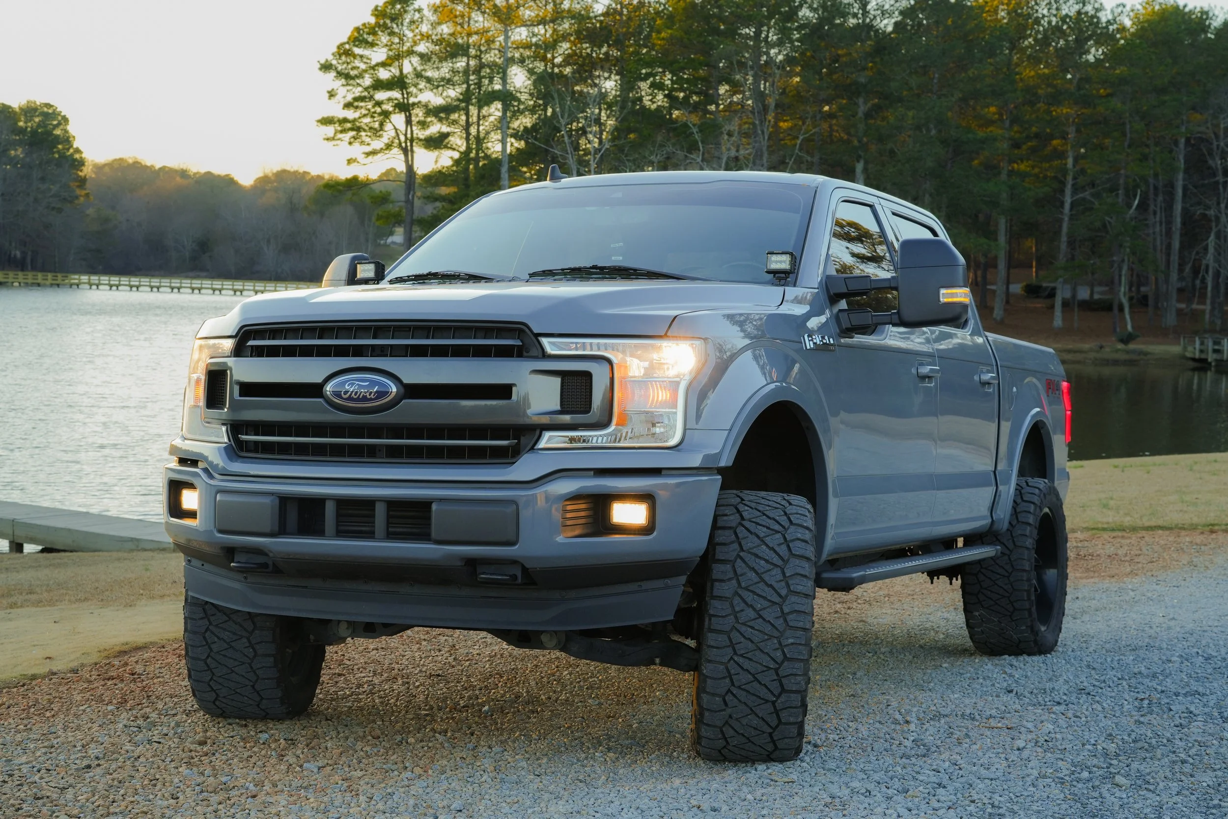 Silver Ford pickup truck parked near a lake with trees in the background during sunset.