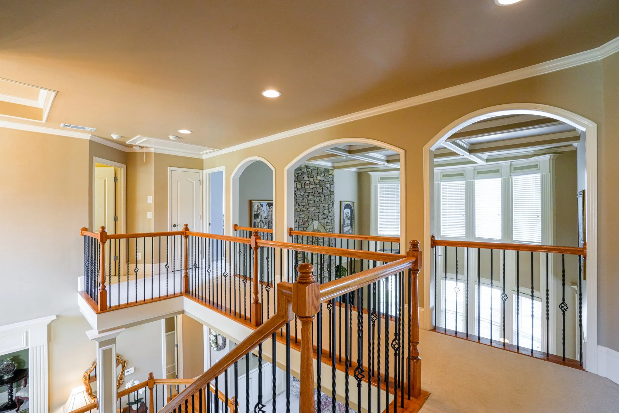 Interior view of a house with a staircase, wooden railing, and multiple windows with blinds.