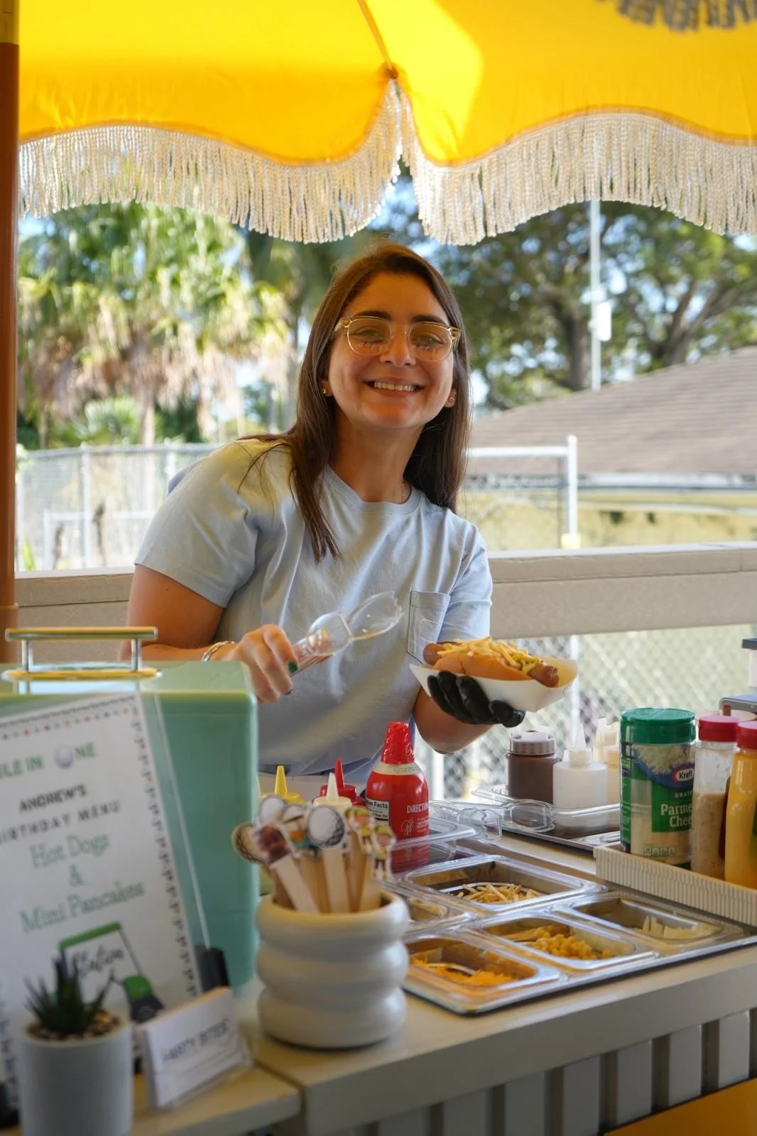 Smiling woman serving hot dog with condiments at outdoor hot dog stand