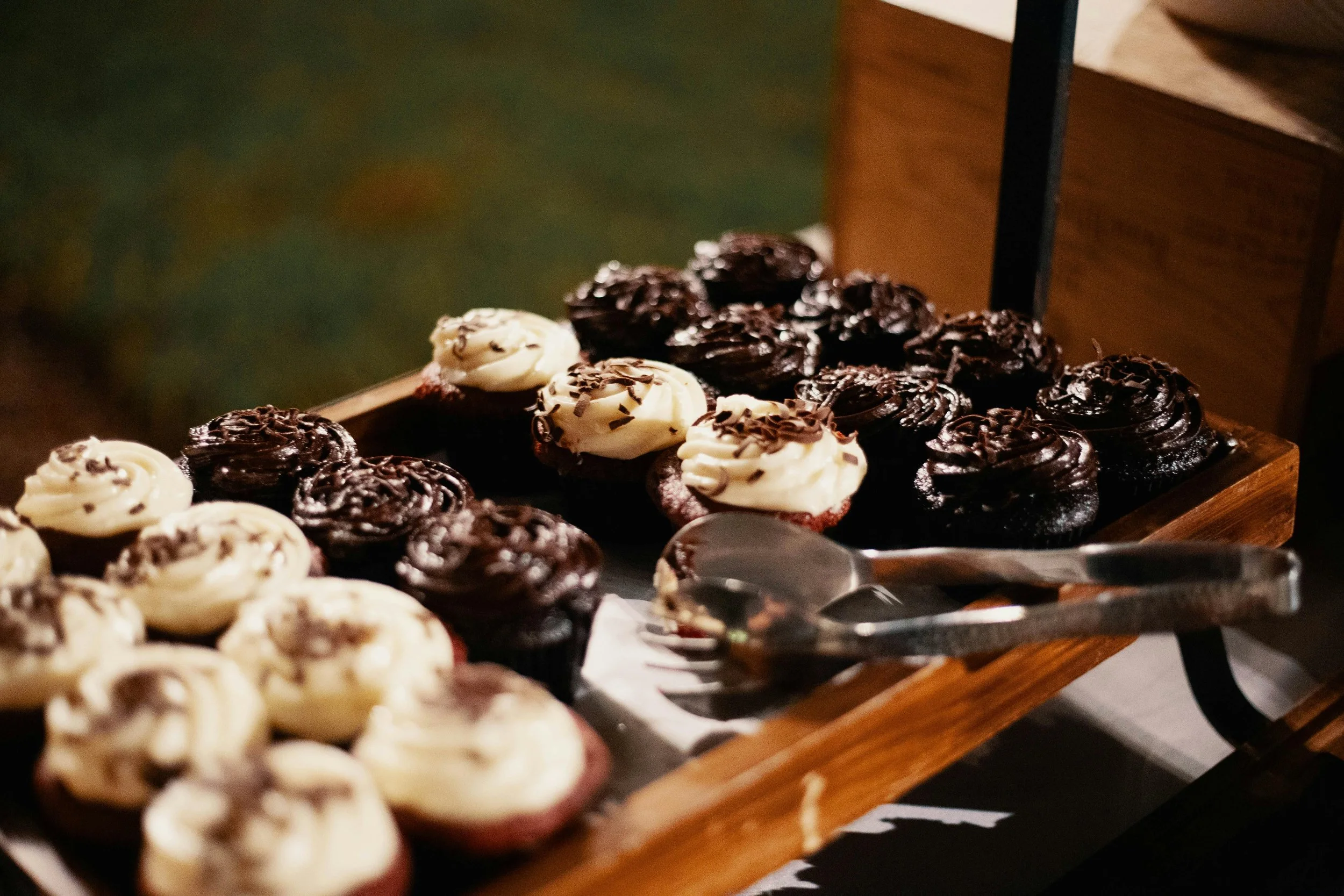 Assorted cupcakes with white and chocolate frosting on a wooden display tray.
