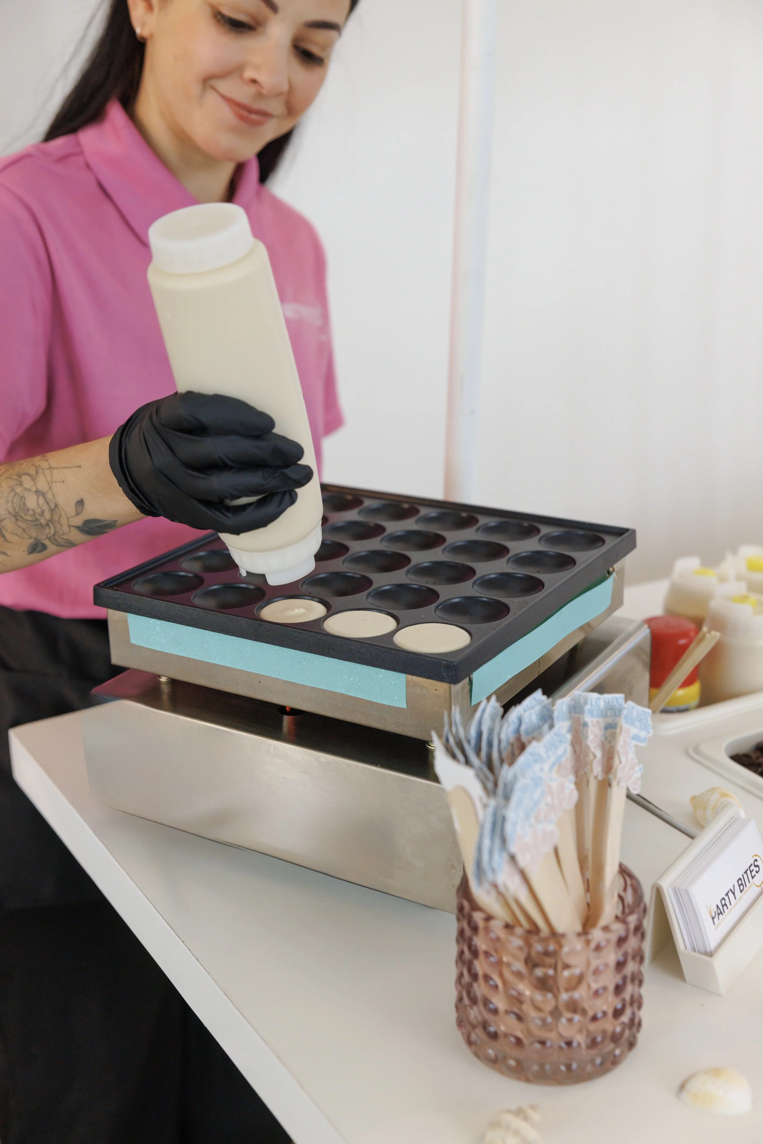 A woman, Lorena, founder of Party Bites MIA in Florida Miami USA in a pink shirt and black gloves is filling an ice cream or dessert mold with white liquid from a squeeze bottle. 