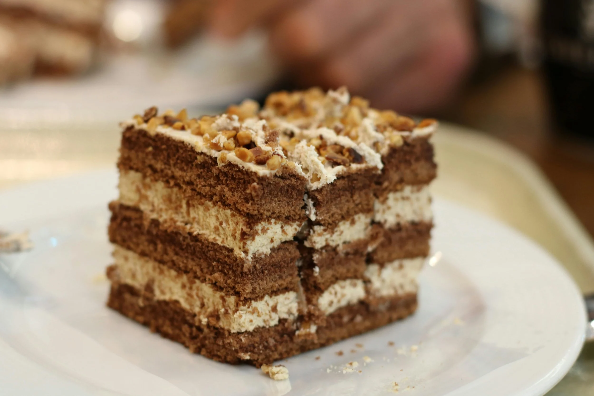 A slice of layered chocolate and vanilla cake with chopped nuts on top on a white plate.