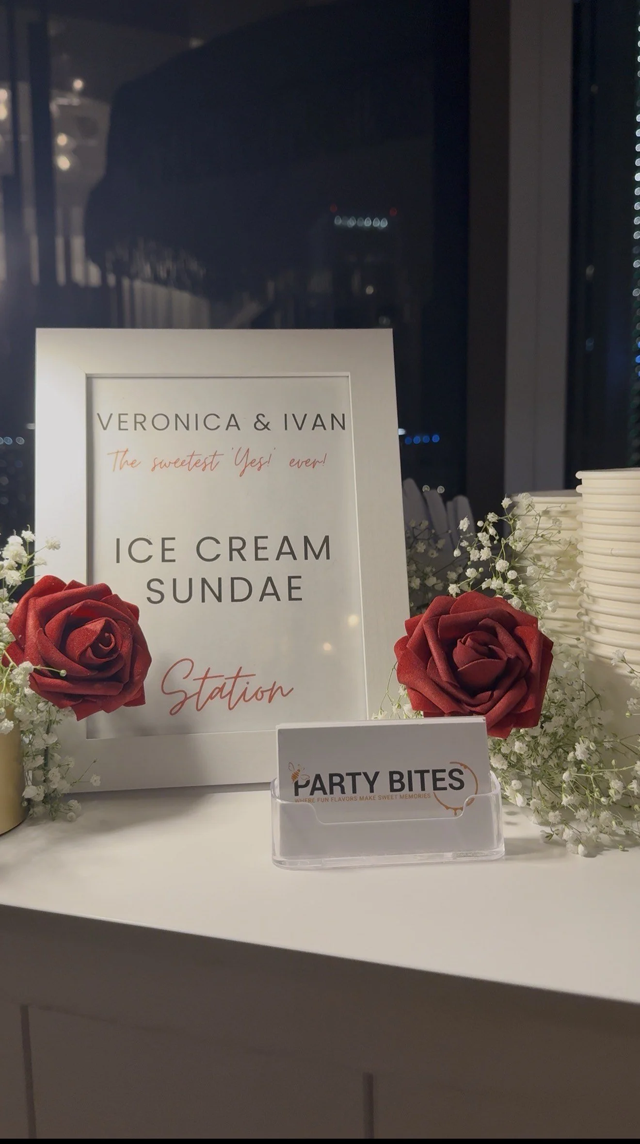 Sign for Veronica & Ivan's ice cream sundae station with red roses and white baby's breath flowers.