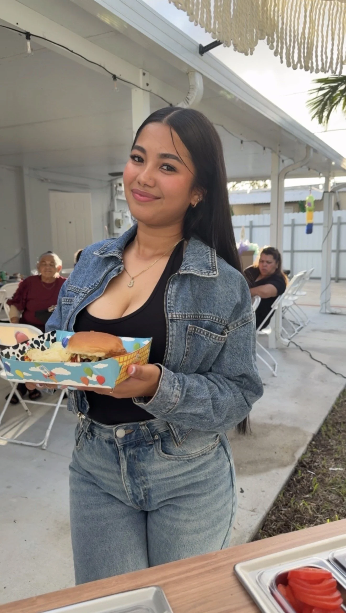 Young woman holding a tray with a burger and chips at an outdoor gathering.