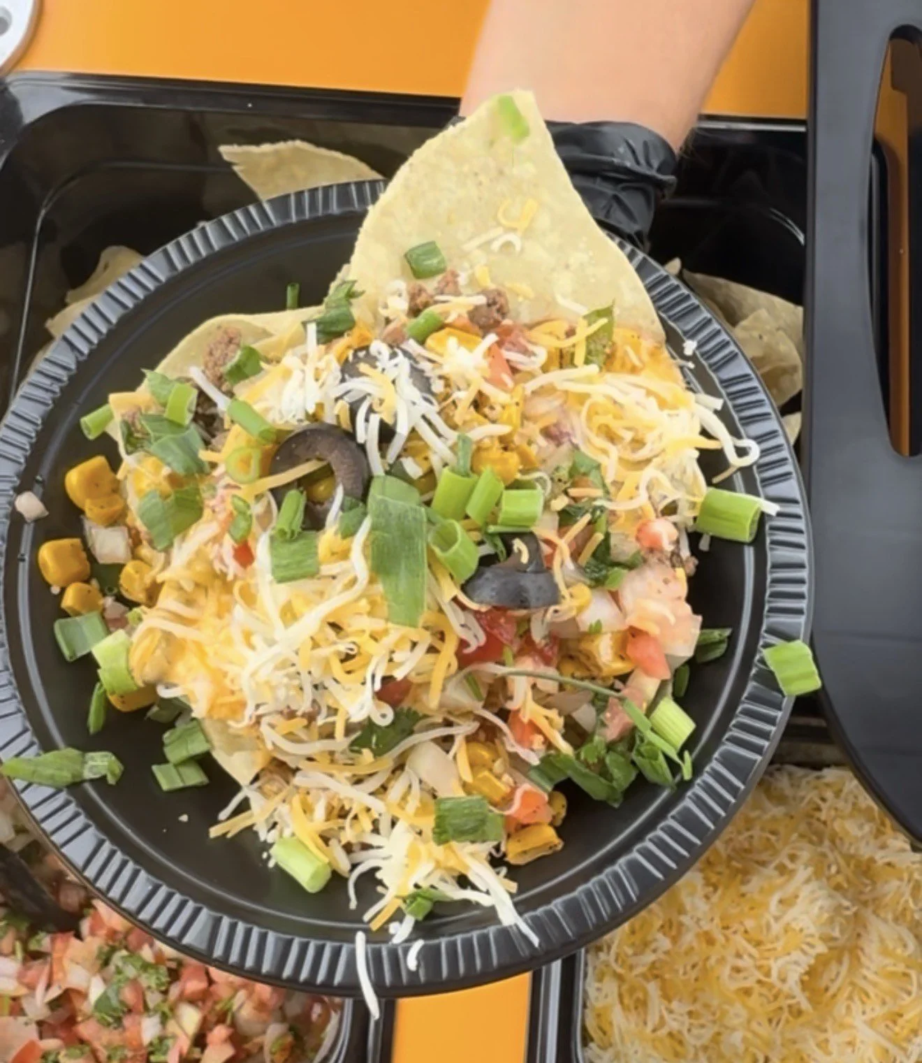 A plate of taco salad with shredded cheese, chopped green onions, black olives, tomatoes, ground beef, and tortilla chips.