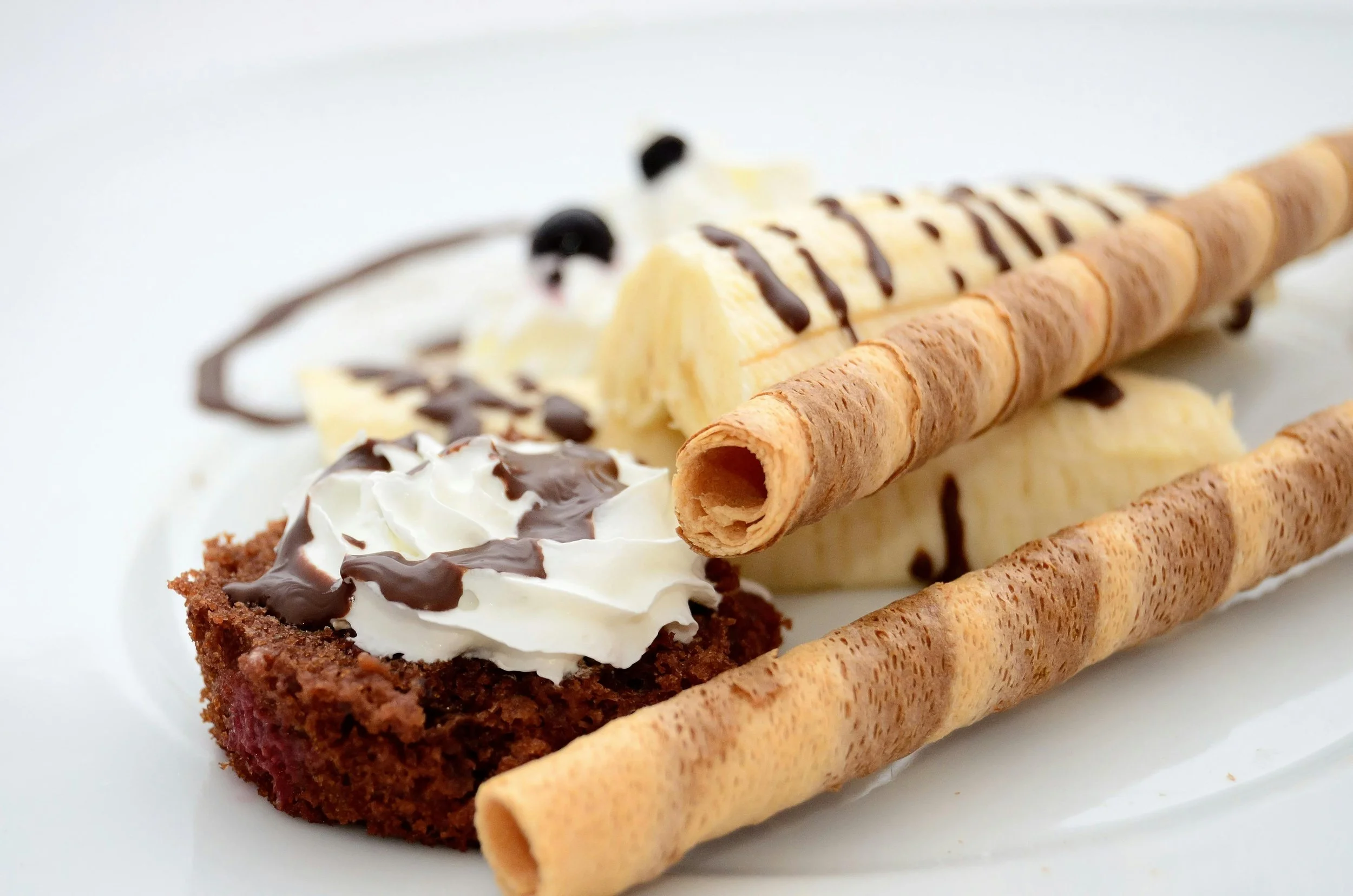 Chocolate brownie with whipped cream and chocolate drizzle, banana slices, Twister ice cream cones, and chocolate topping on bananas, all on a white plate.