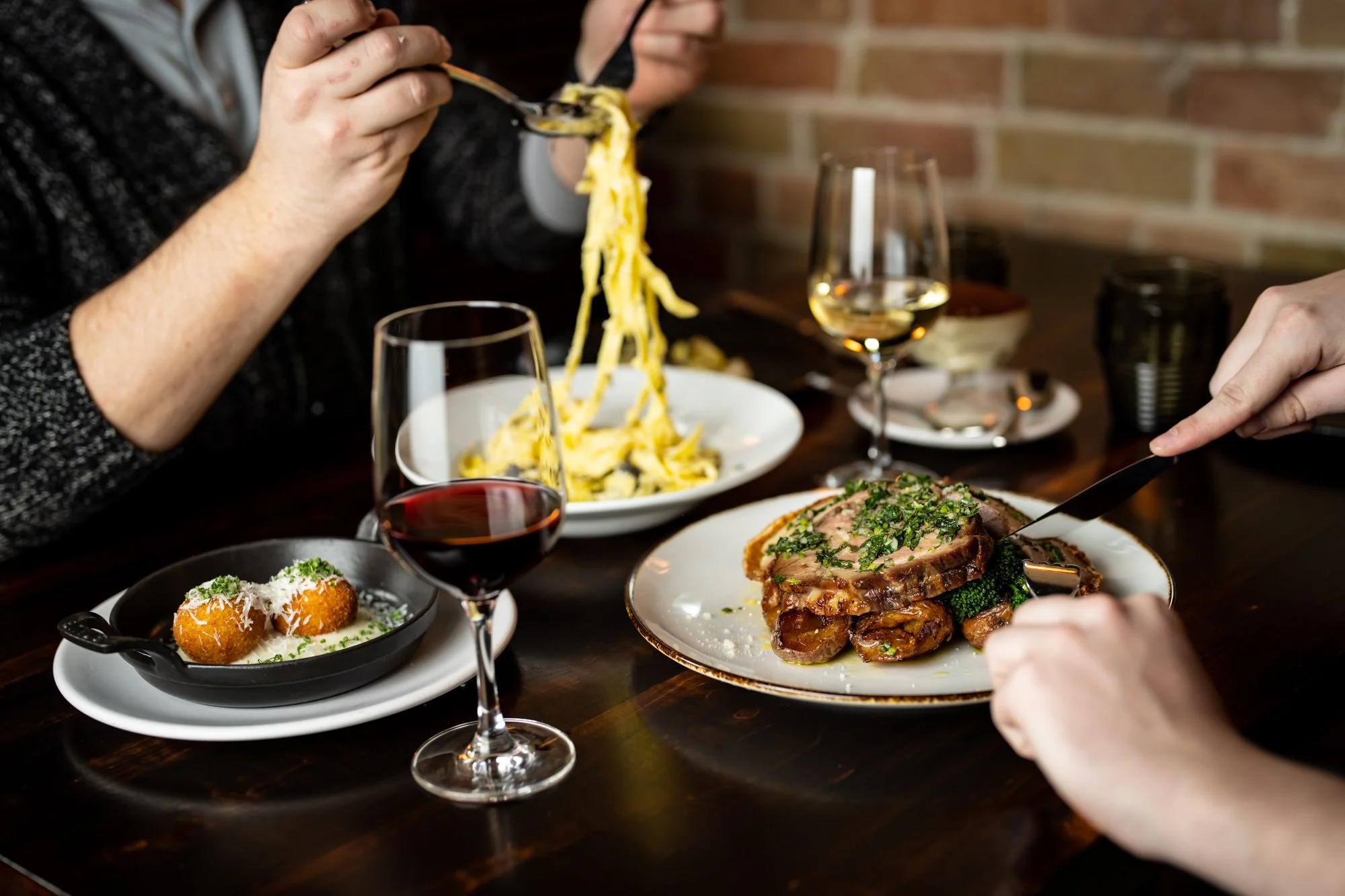 Shared dinner table with pasta, a meat main, arancini, and wine at The Berczy Tavern, a New Canadian bistro and piano bar in downtown Toronto