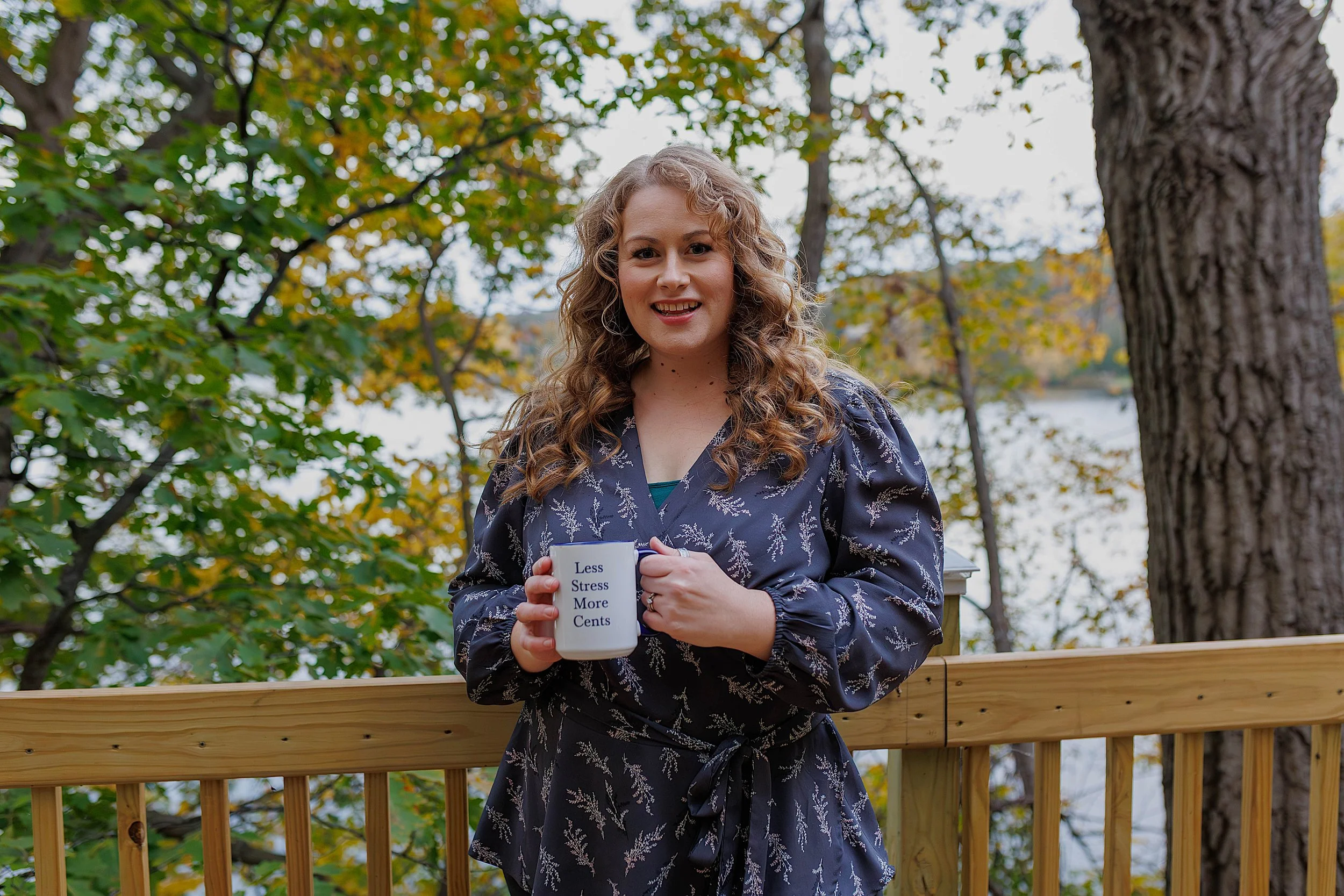 Natasha Bradt, Founder of 3 Lakes Bookkeeping, holding a branded coffee mug while standing on an outdoor wooden deck with a scenic lake background, answering QuickBooks Online and virtual accounting FAQs