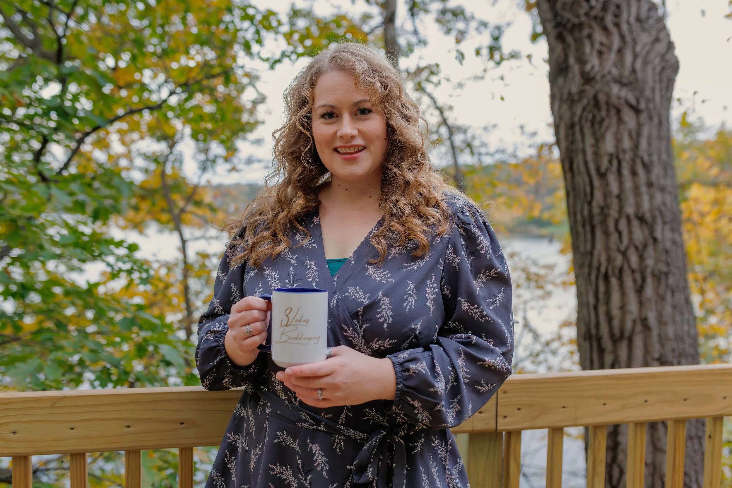 Natasha Bradt, Founder of 3 Lakes Bookkeeping, smiling and holding a coffee mug outdoors, inviting small business owners to schedule a free bookkeeping consultation call.