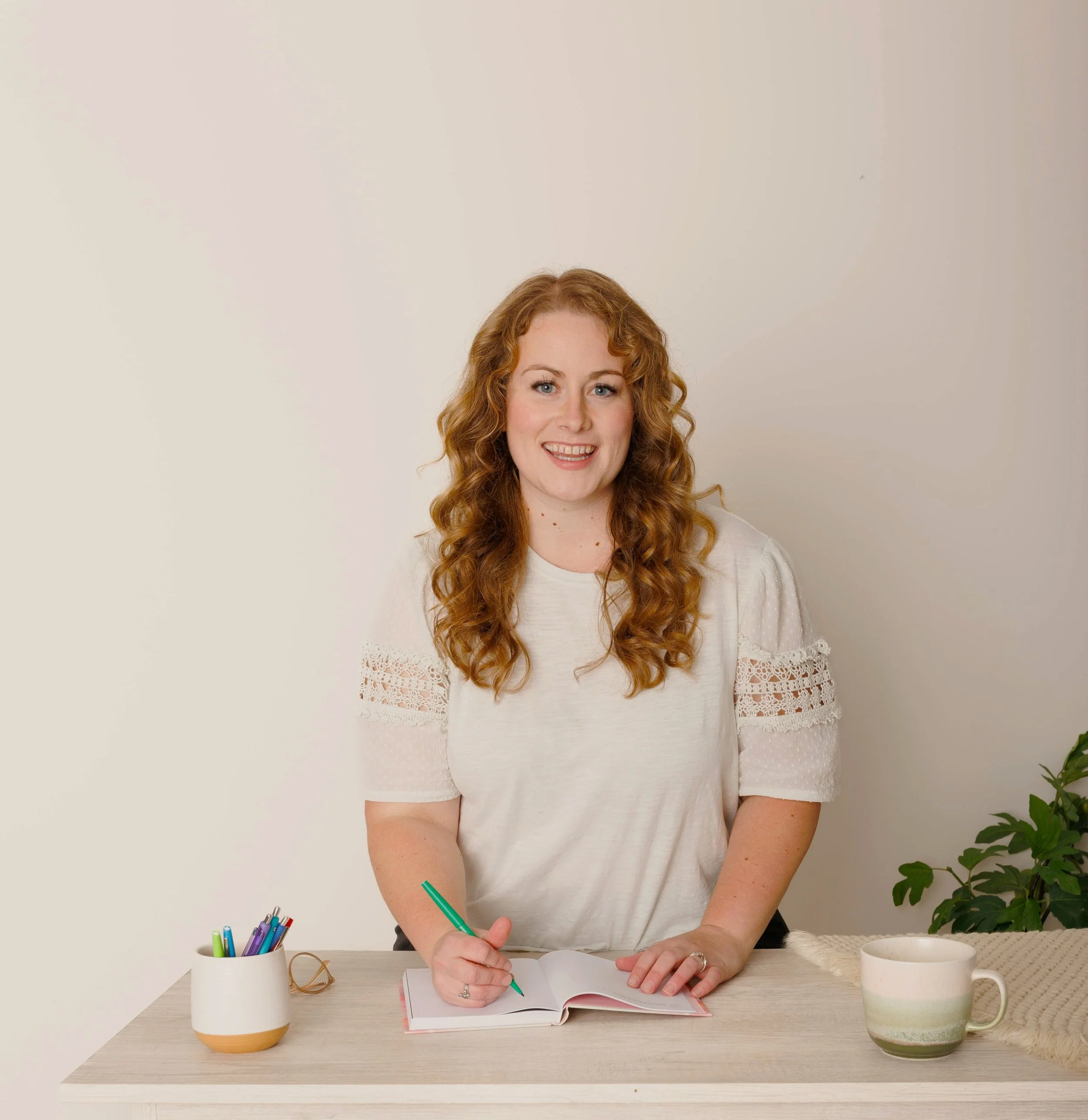 Smiling professional Natasha Bradt, Founder of 3 Lakes Bookkeeping, seated at a desk writing in a notebook, offering virtual bookkeeping and remote accounting services for small businesses.