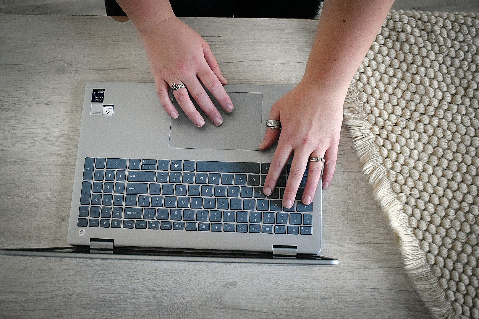 Top-down view of a remote bookkeeper's hands using a laptop trackpad and keyboard, managing online financial records and communication for small business clients.