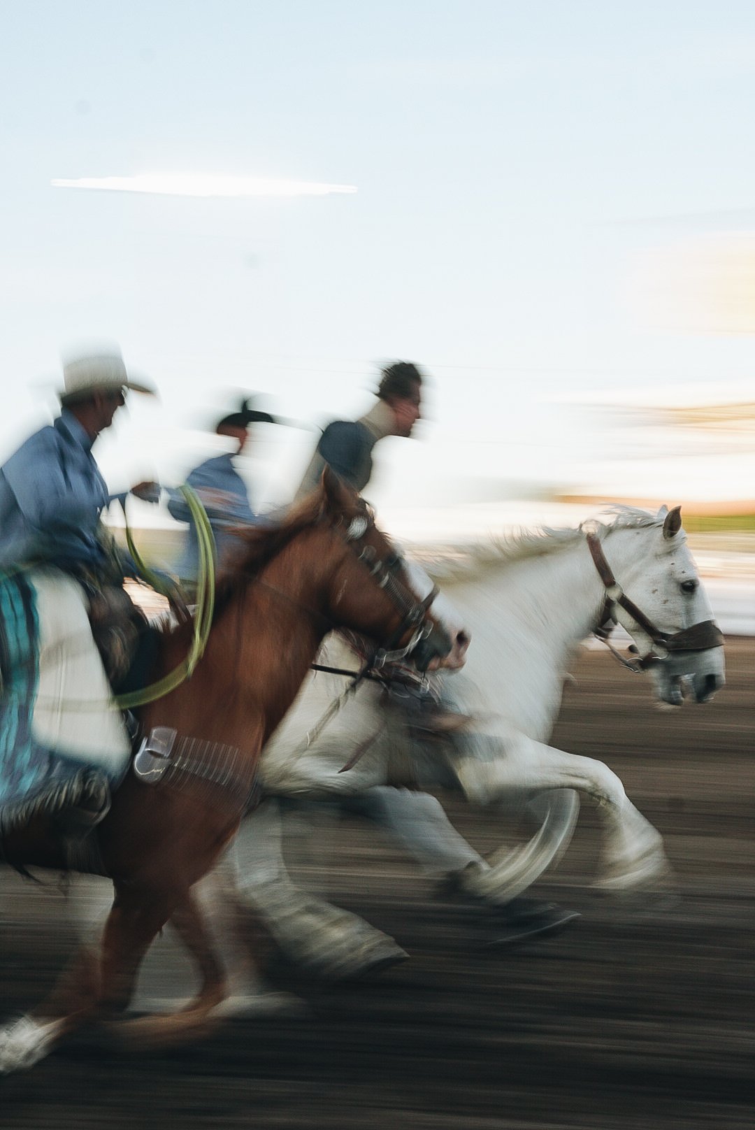 Three blurred cowboys on horses at a rodeo event
