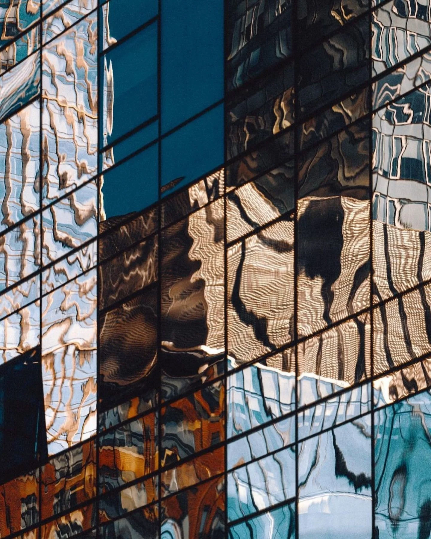 Reflections of buildings on a glass facade showing distorted patterns and colors of the surrounding structures.