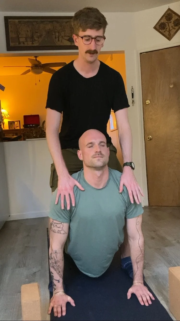 Private yoga instructor Jimmie Costello providing a hands-on shoulder adjustment for an inflexible man during an in-home session in Manhattan.