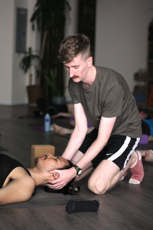 A man is practicing CPR on a woman lying on the floor in a fitness or yoga studio with yoga mats and water bottles in the background.