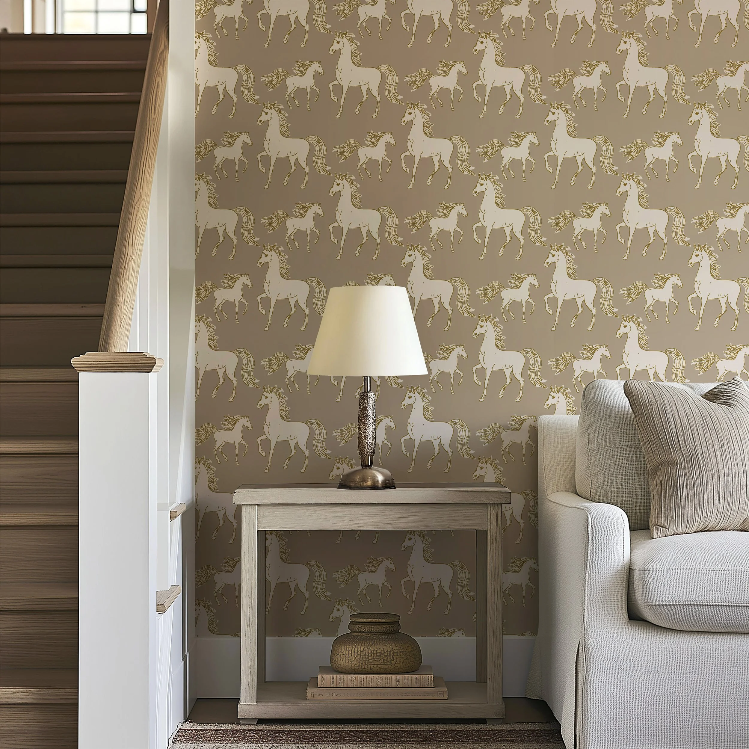 Living room corner with beige wallpaper featuring white and gold horses, a white side table with a lamp, a beige couch with pillows, and a stairway nearby.