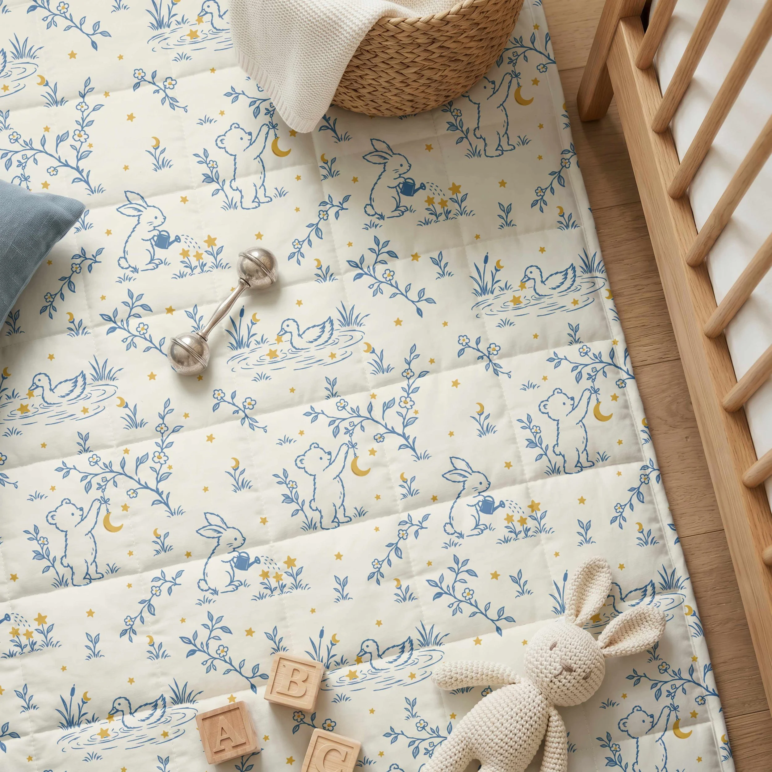 Dusty blue and golden yellow woodland nursery fabric featuring playful rabbits, a bear, ducks, crescent moons, and stars, styled with wooden toys and a knitted bunny.