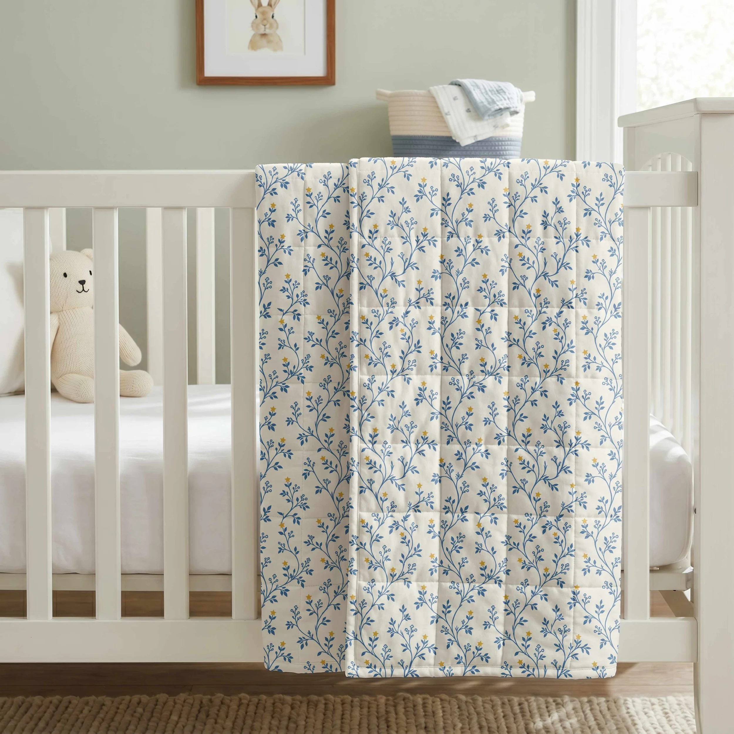Blue botanical star vine nursery print with delicate leafy branches and golden yellow stars, displayed on a baby blanket draped over a white crib in a neutral nursery.