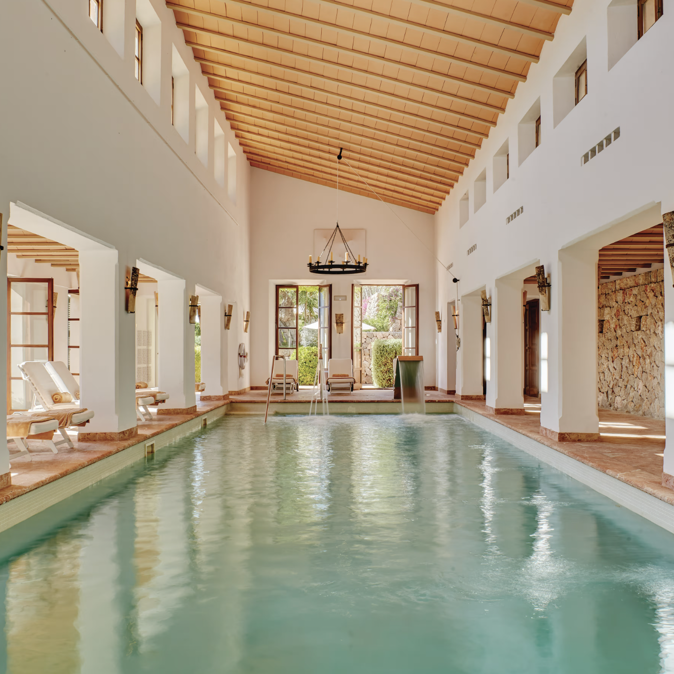 Indoor swimming pool with large windows, wooden ceiling, and comfortable lounge chairs.