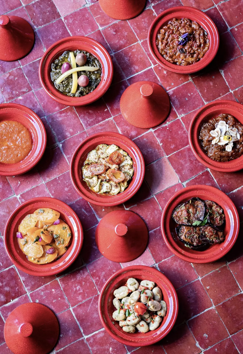 Several traditional Mexican dishes served in red ceramic bowls arranged on a red tiled table.