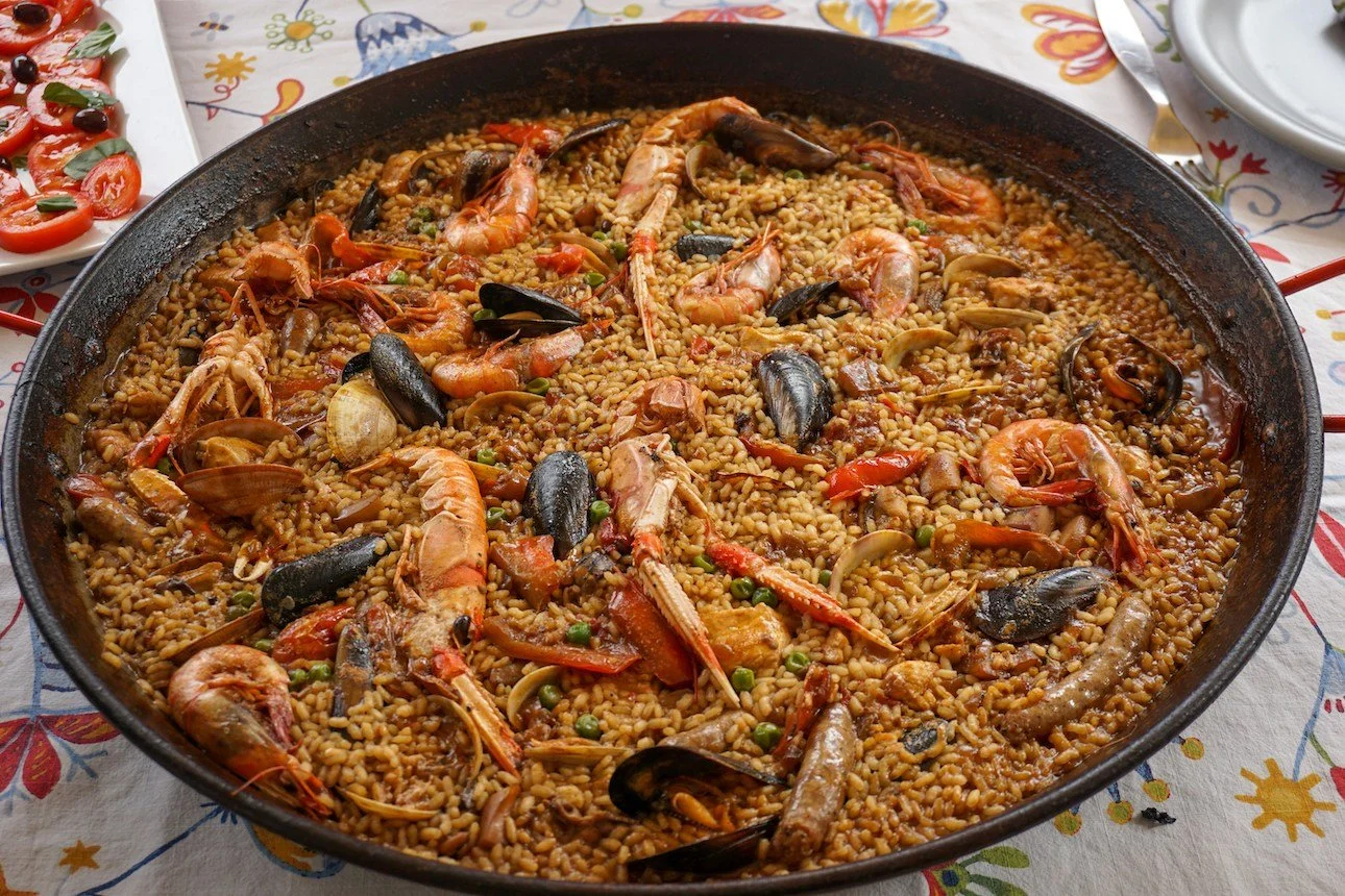 Pan of seafood paella with shrimp, mussels, and rice on a decorative tablecloth.