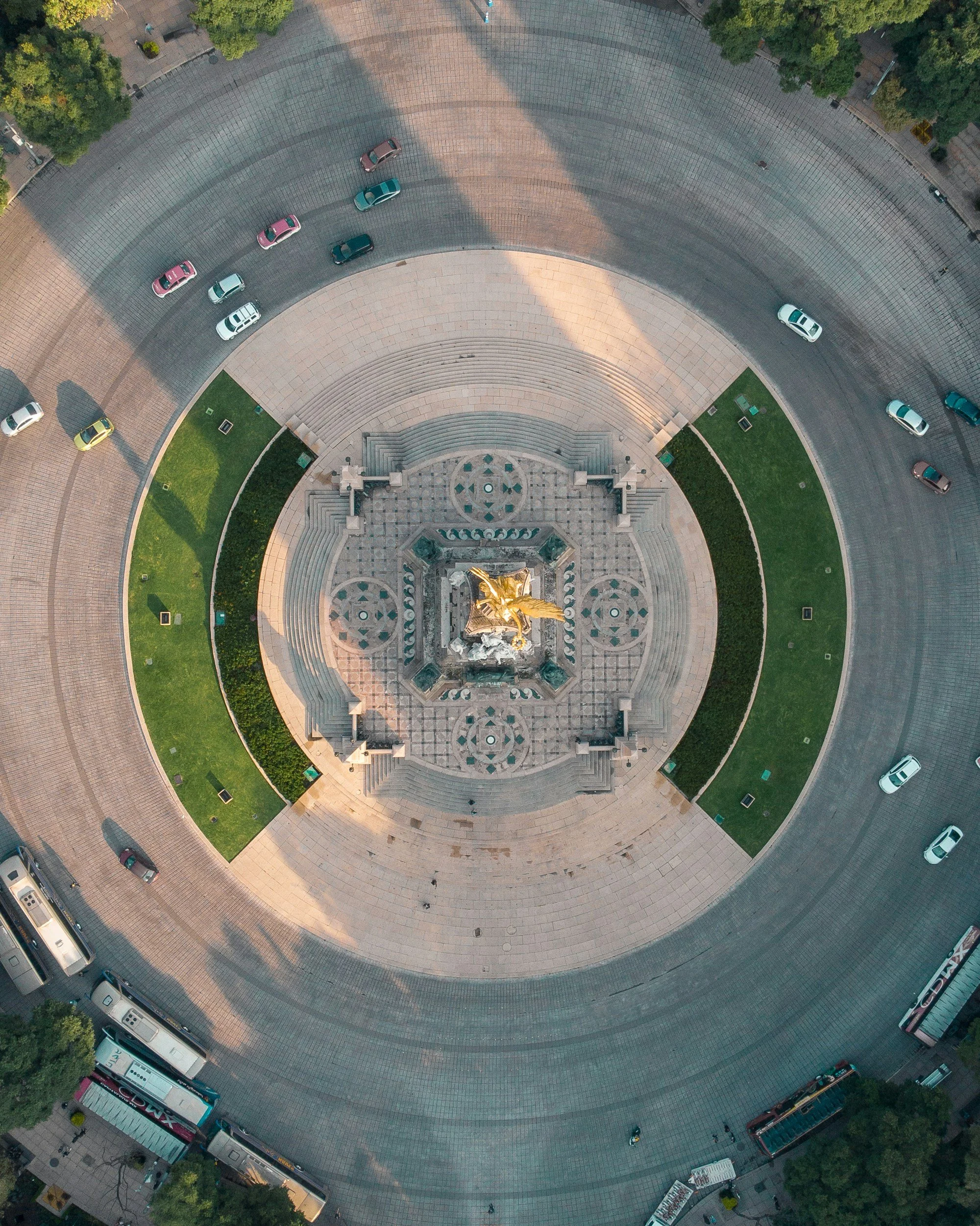 Aerial view of a roundabout with a large sculpture in the center, surrounded by vehicles on the road, and greenery on the edges.