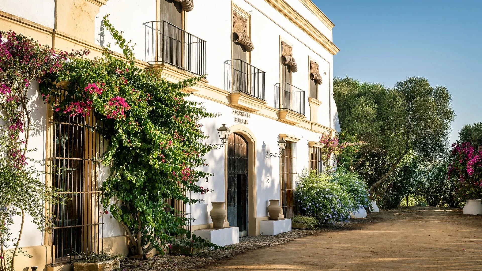 Colorful Spanish-style buildings with balconies, decorative metalwork, and potted plants; signs for Casa Román, Hosteria del Laurel, and Restaurant visible.