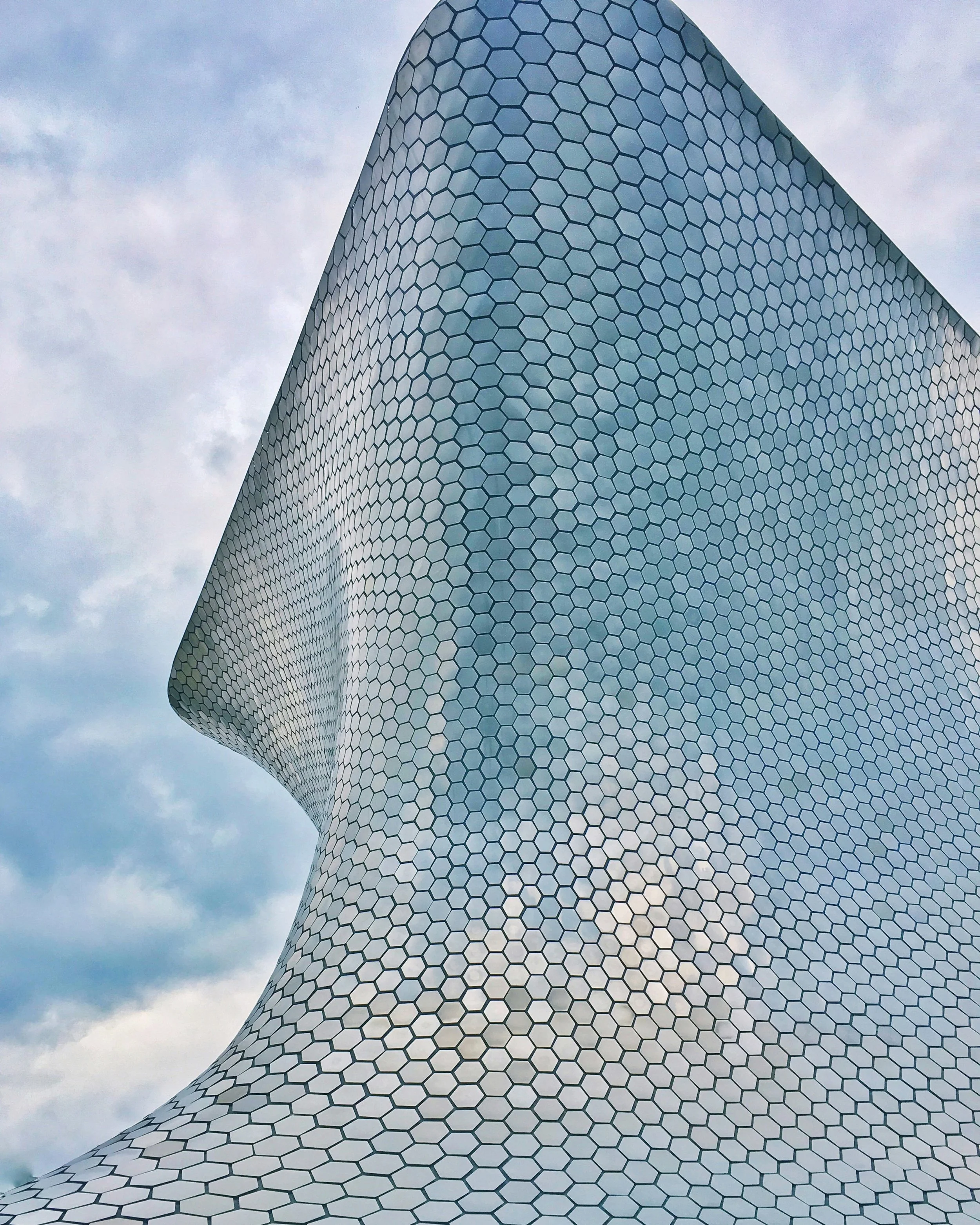 Modern building with hexagonal panel facade against cloudy sky.