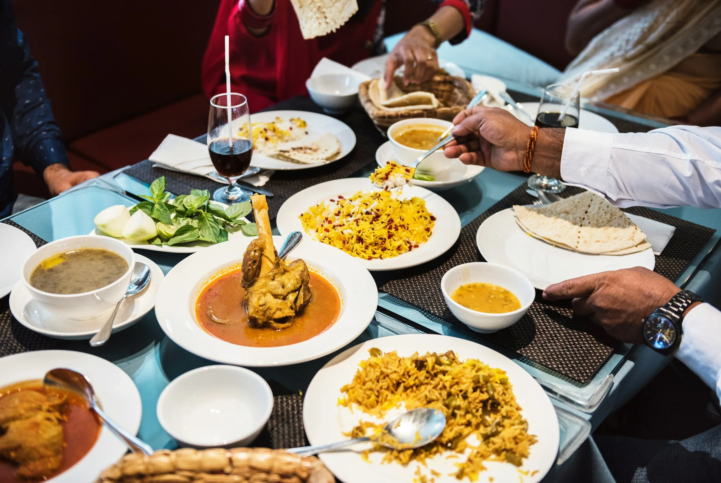 Table with Indian dishes including curry, dal, rice, naan, and drinks.