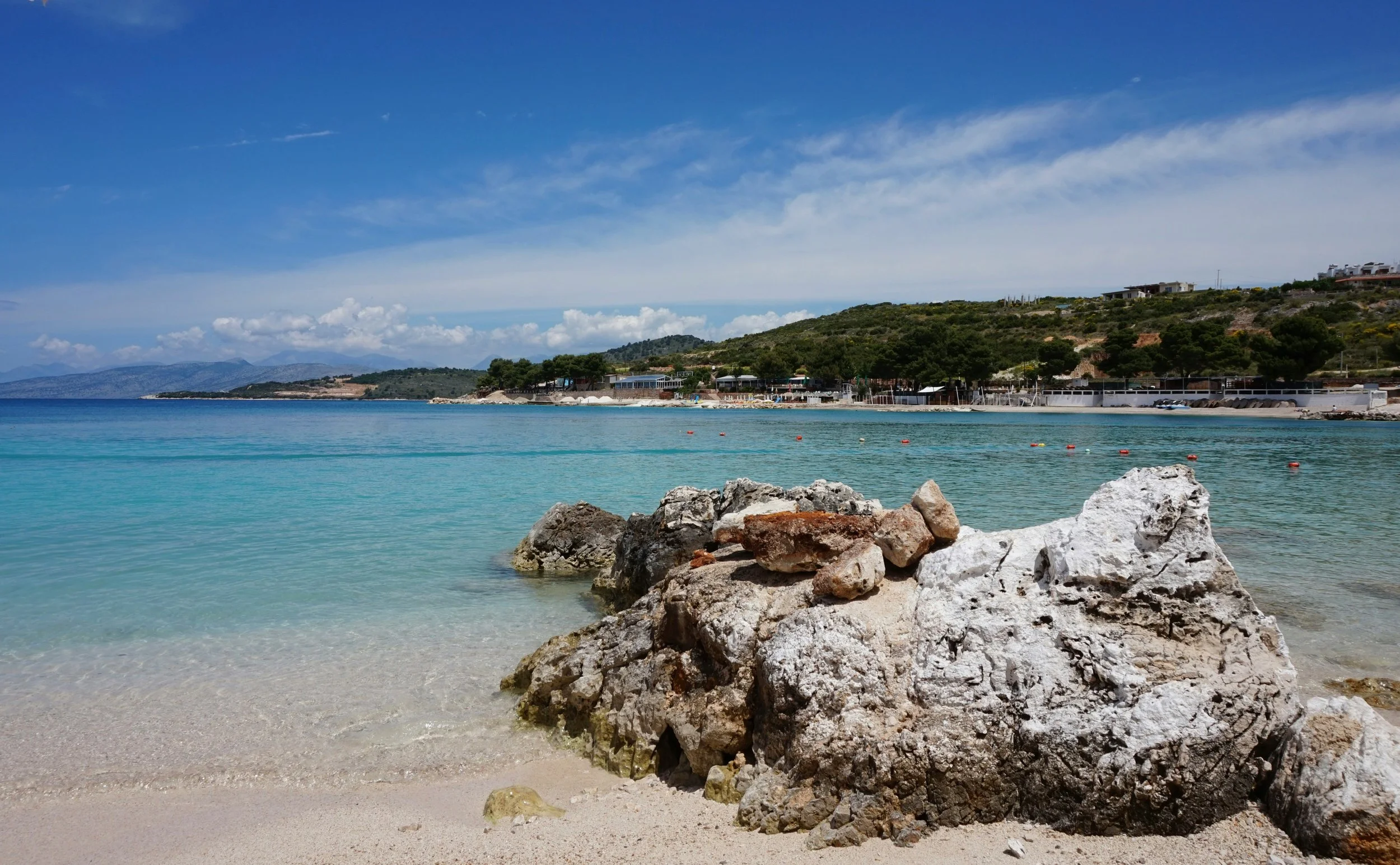 A scenic beach featuring rocks and calm water in the foreground, with gentle waves lapping at the shore.