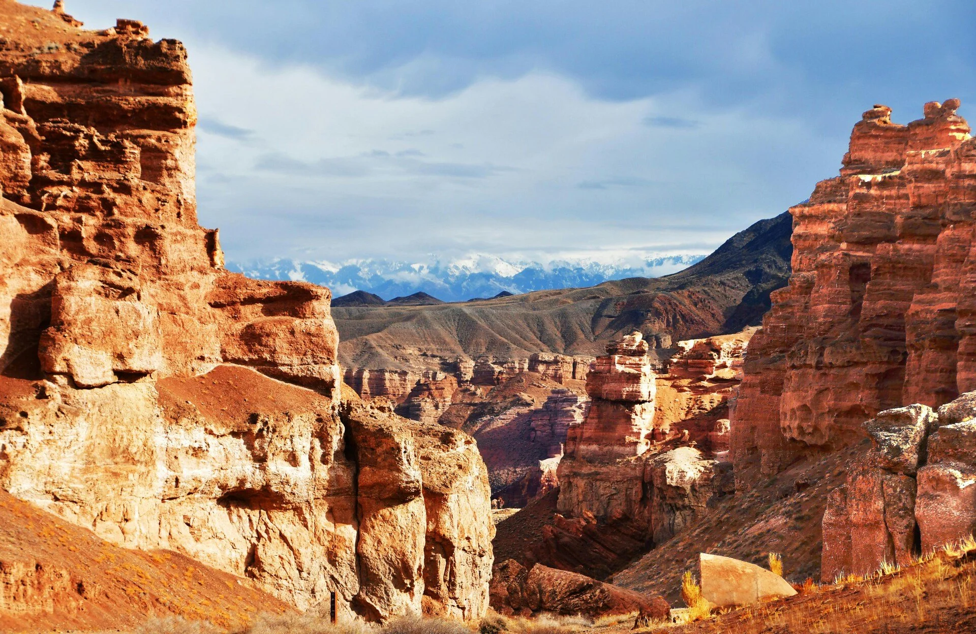 A desert landscape with layered rock formations and plateaus, under a cloudy sky.