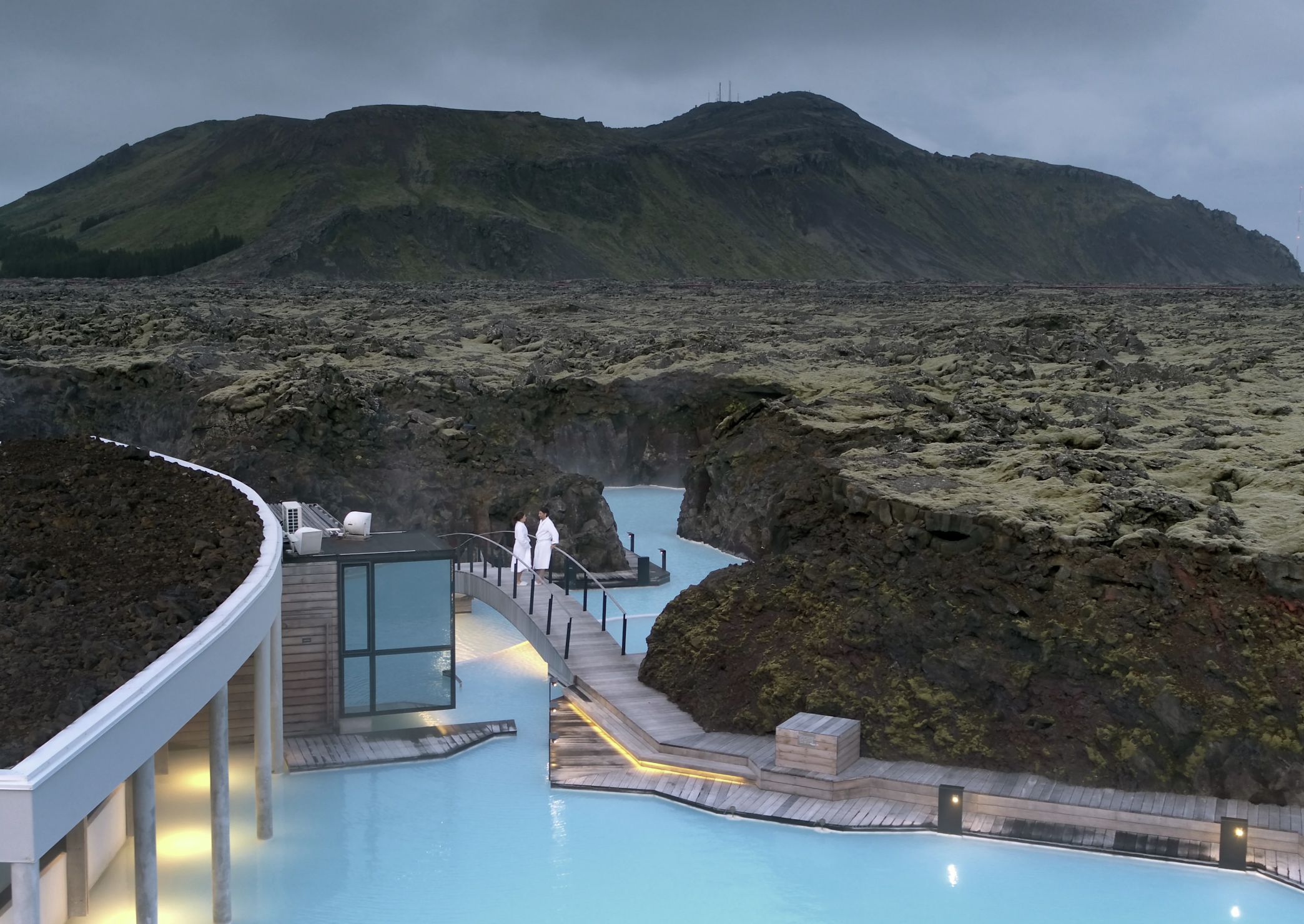 Geothermal spa with blue water, surrounded by volcanic rocks and mountainous landscape.