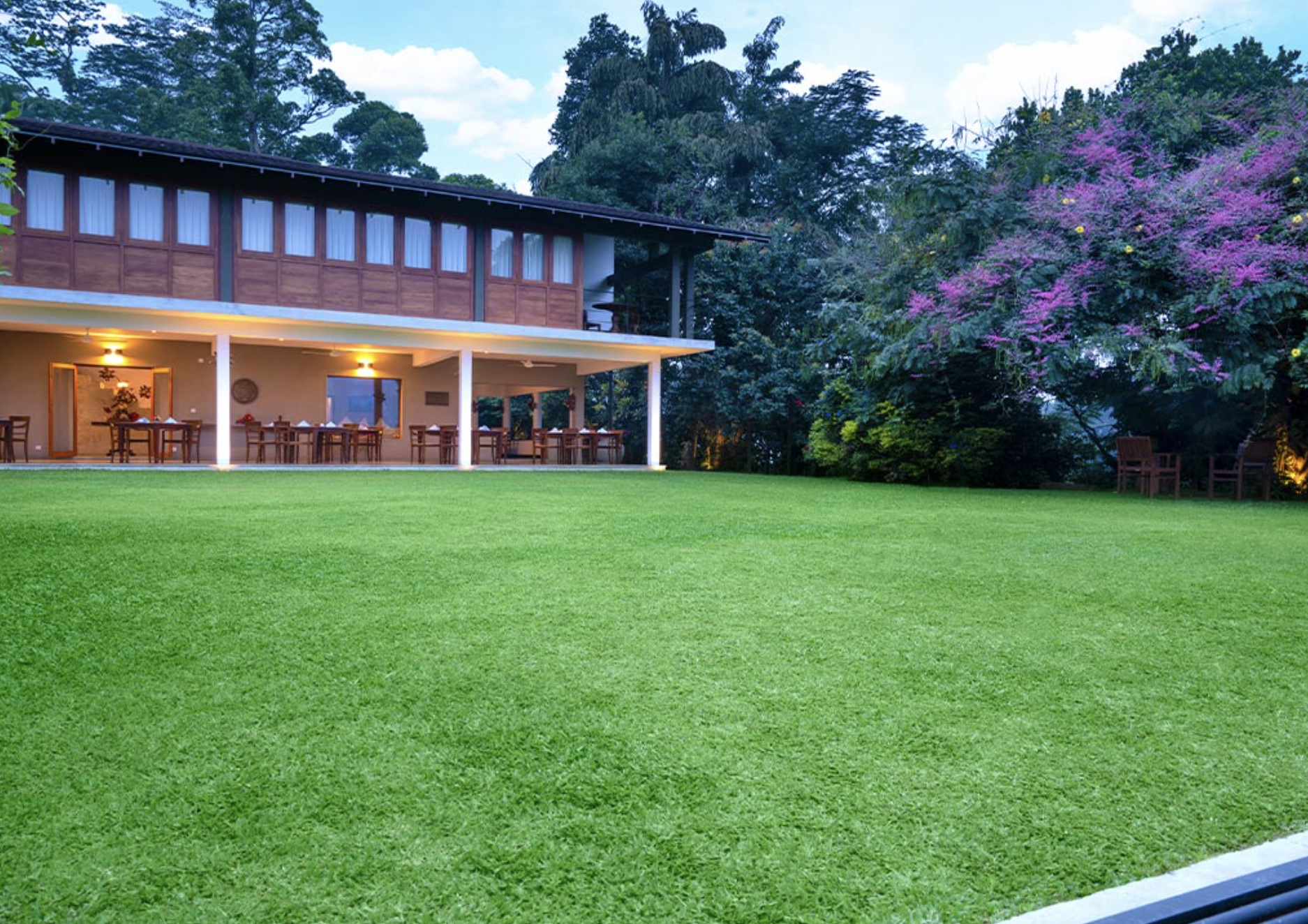 Two-story building with outdoor seating and lush green lawn, surrounded by trees and colorful foliage.