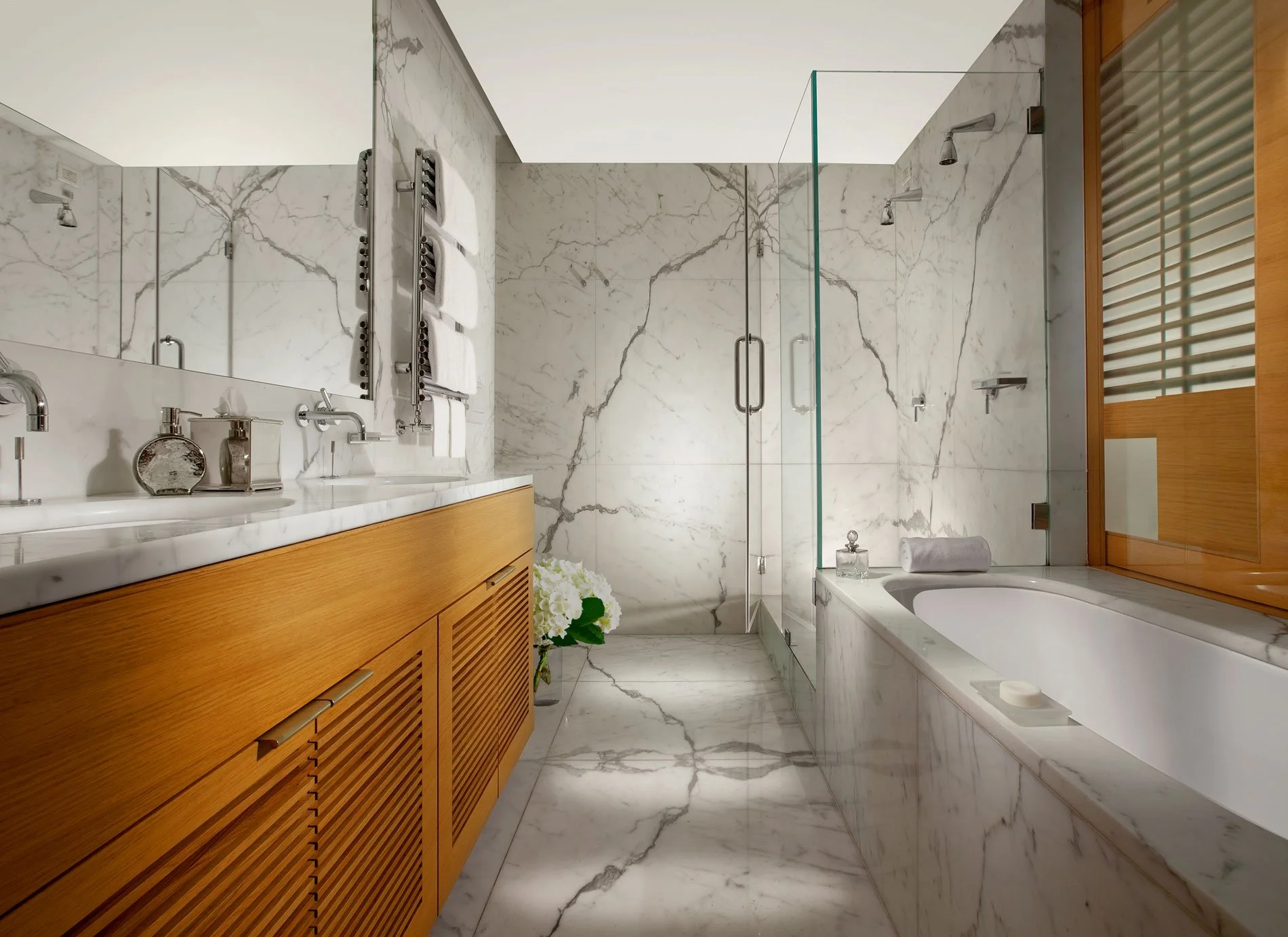 Luxurious bathroom with marble surfaces, a wooden vanity, glass shower, and bathtub.