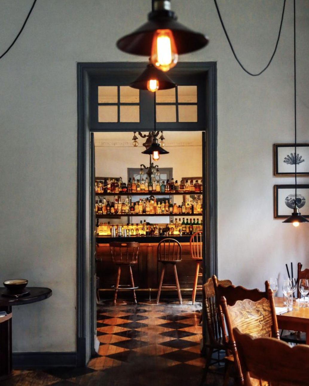Cozy bar room with dim lighting, vintage decor, wooden stools, and a well-stocked liquor shelf.