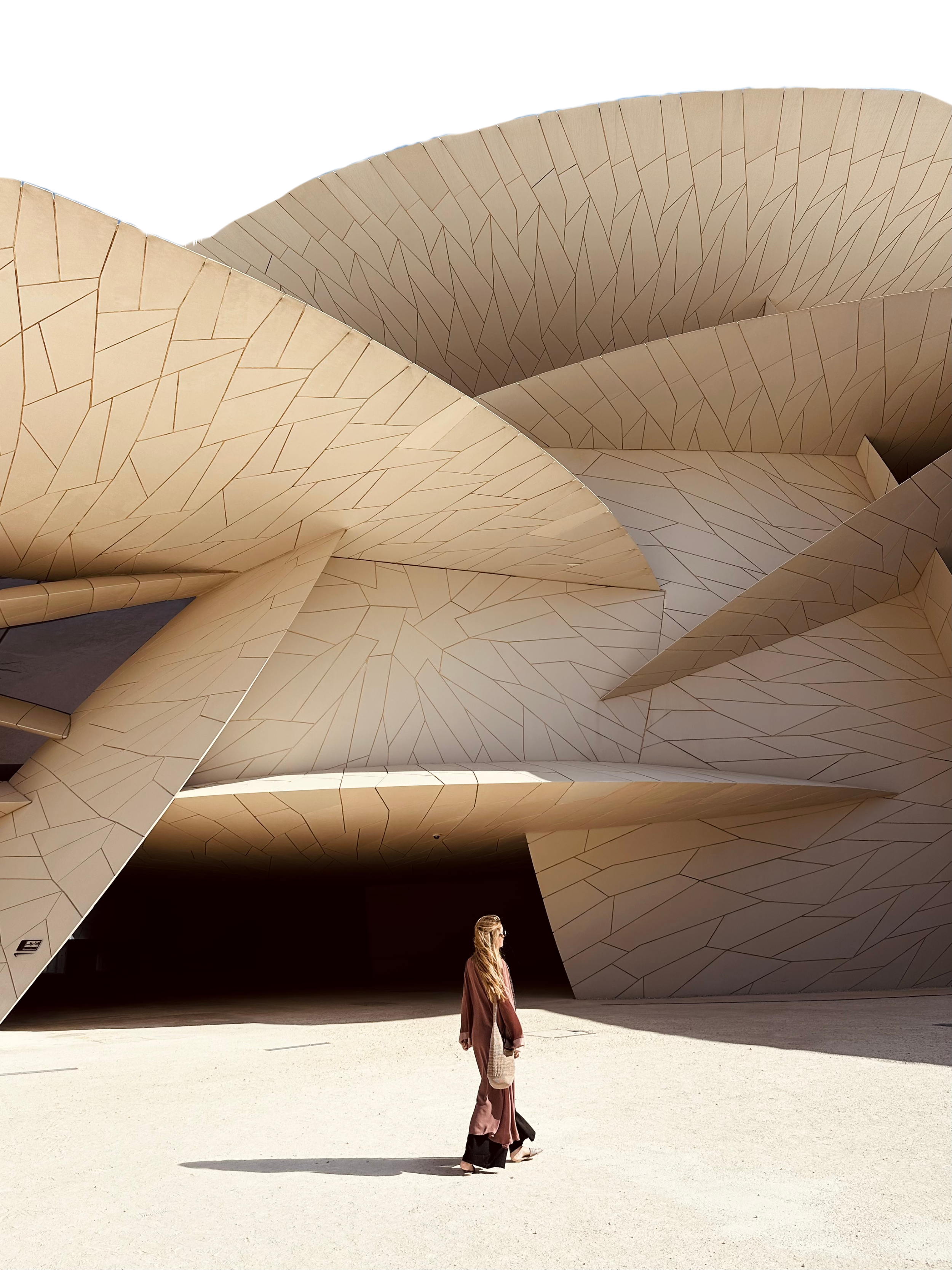 A woman walking in front of a modern, abstract building with curved, angular beige panels.